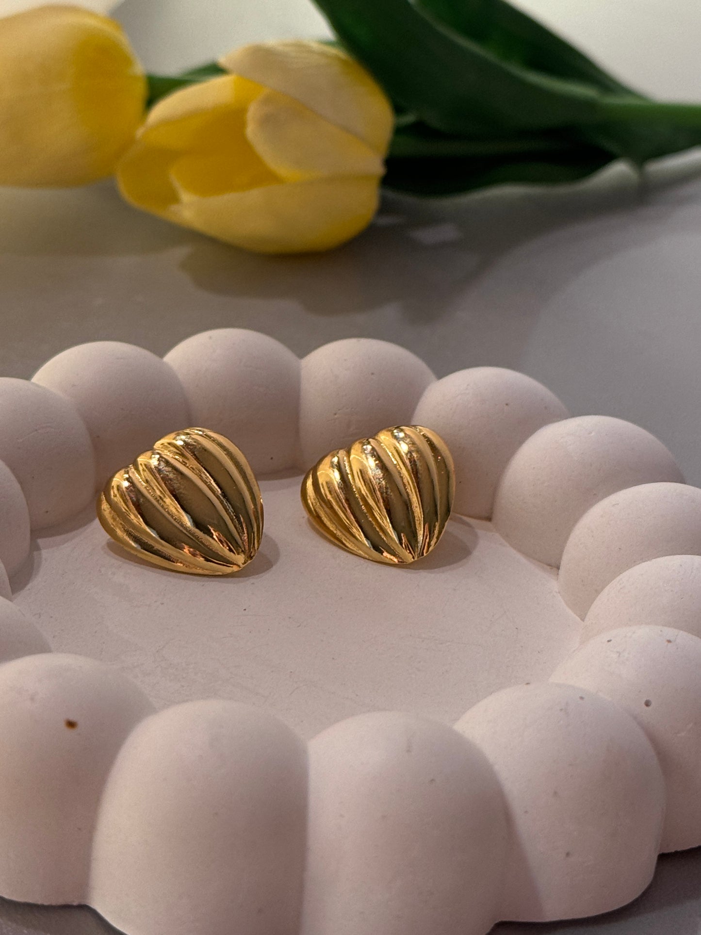Gold earrings on a white textured surface with yellow tulips in the background
