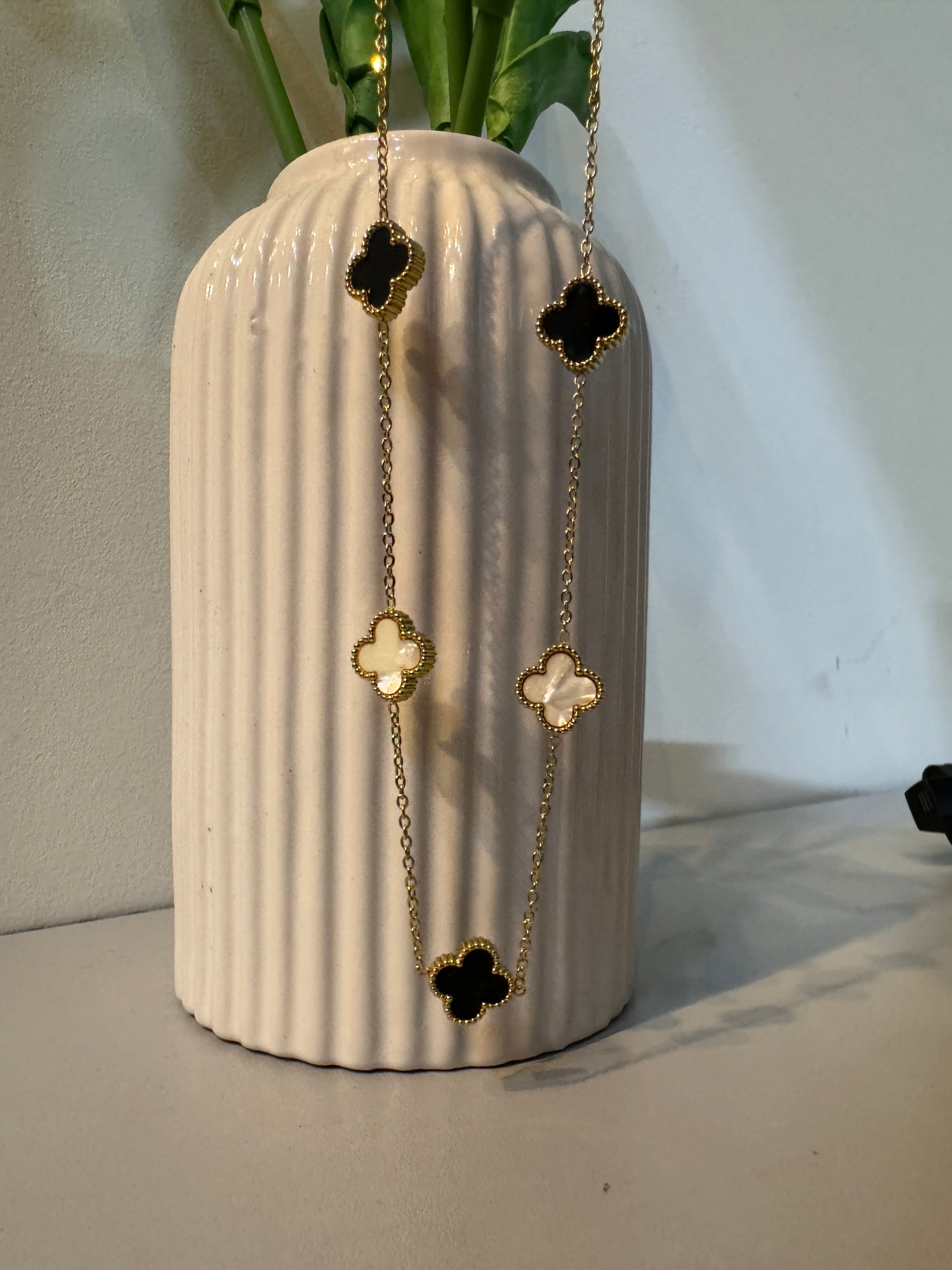 Gold necklace with clover-shaped pendants on a textured white surface