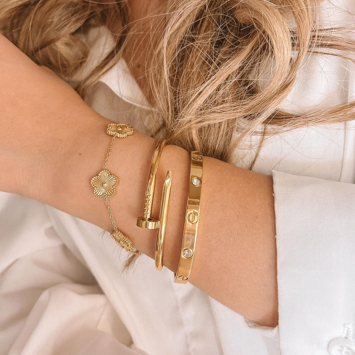 Close-up of a person's arm wearing gold bracelets on a light background