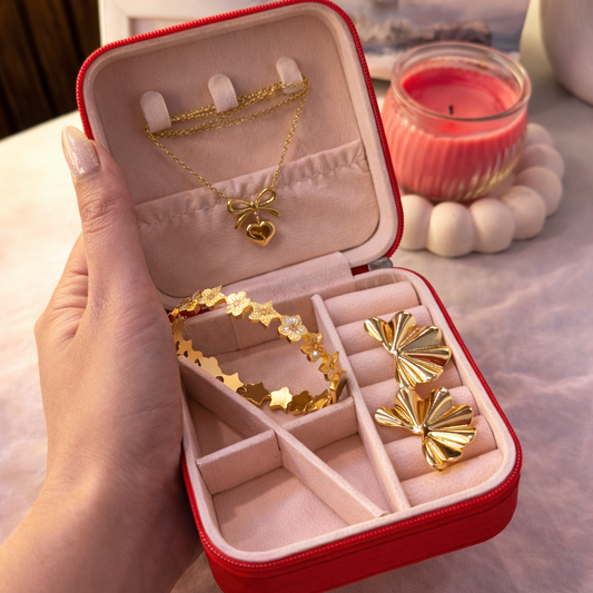 Red jewelry box with gold necklaces and rings held by a hand, with a blurred background.