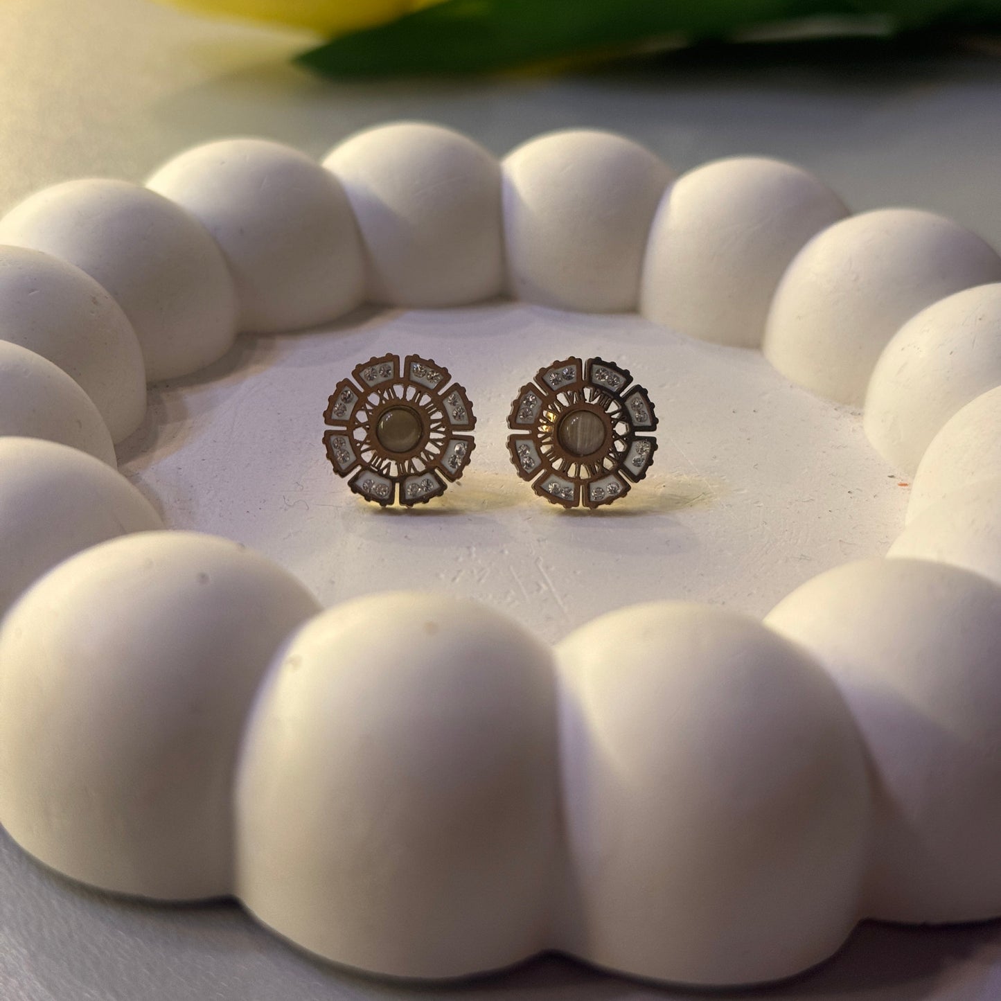 Pair of earrings in a white round frame with a yellow tulip in the background