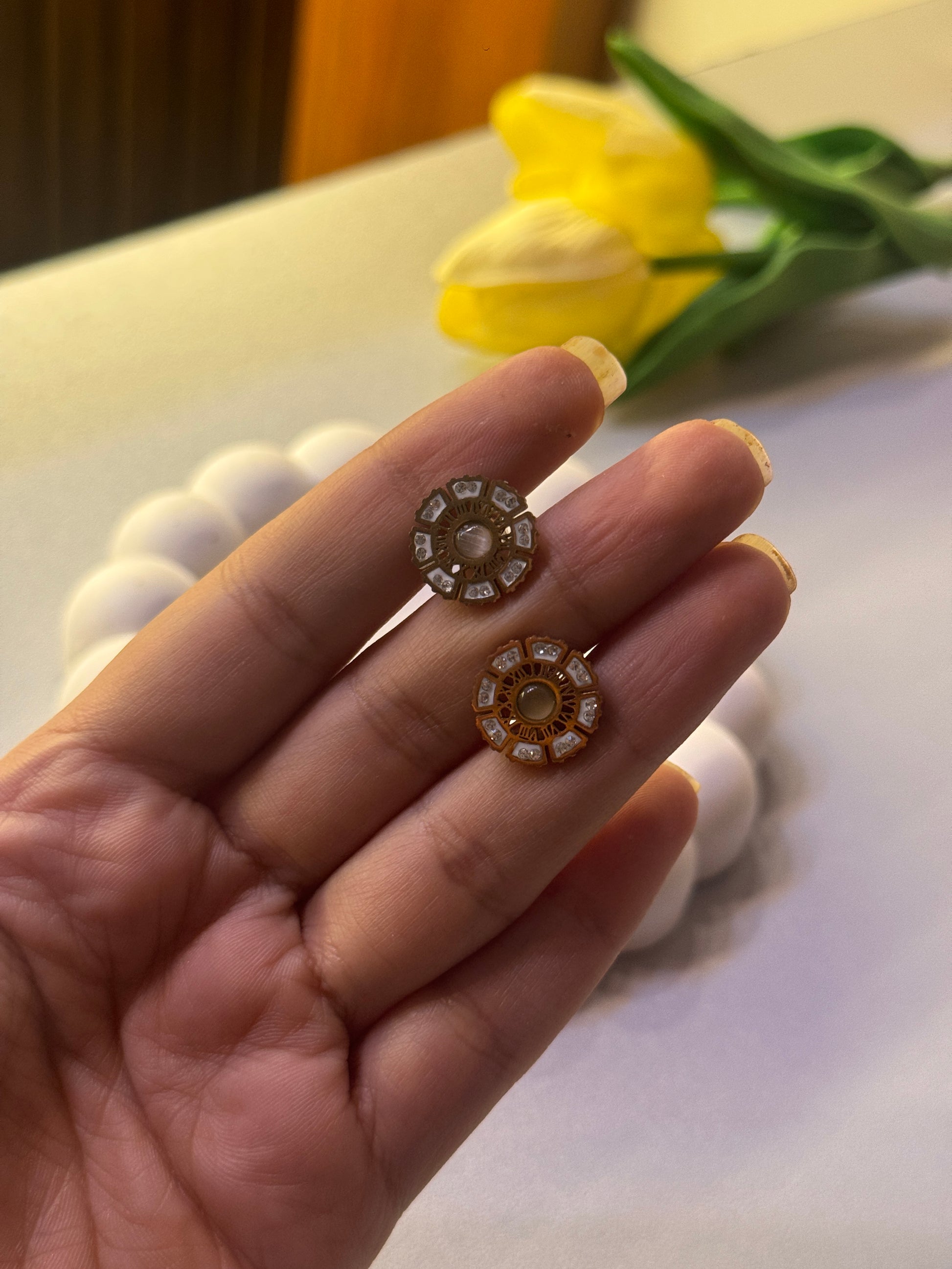 Gold and diamond earrings held between fingers with a blurred background