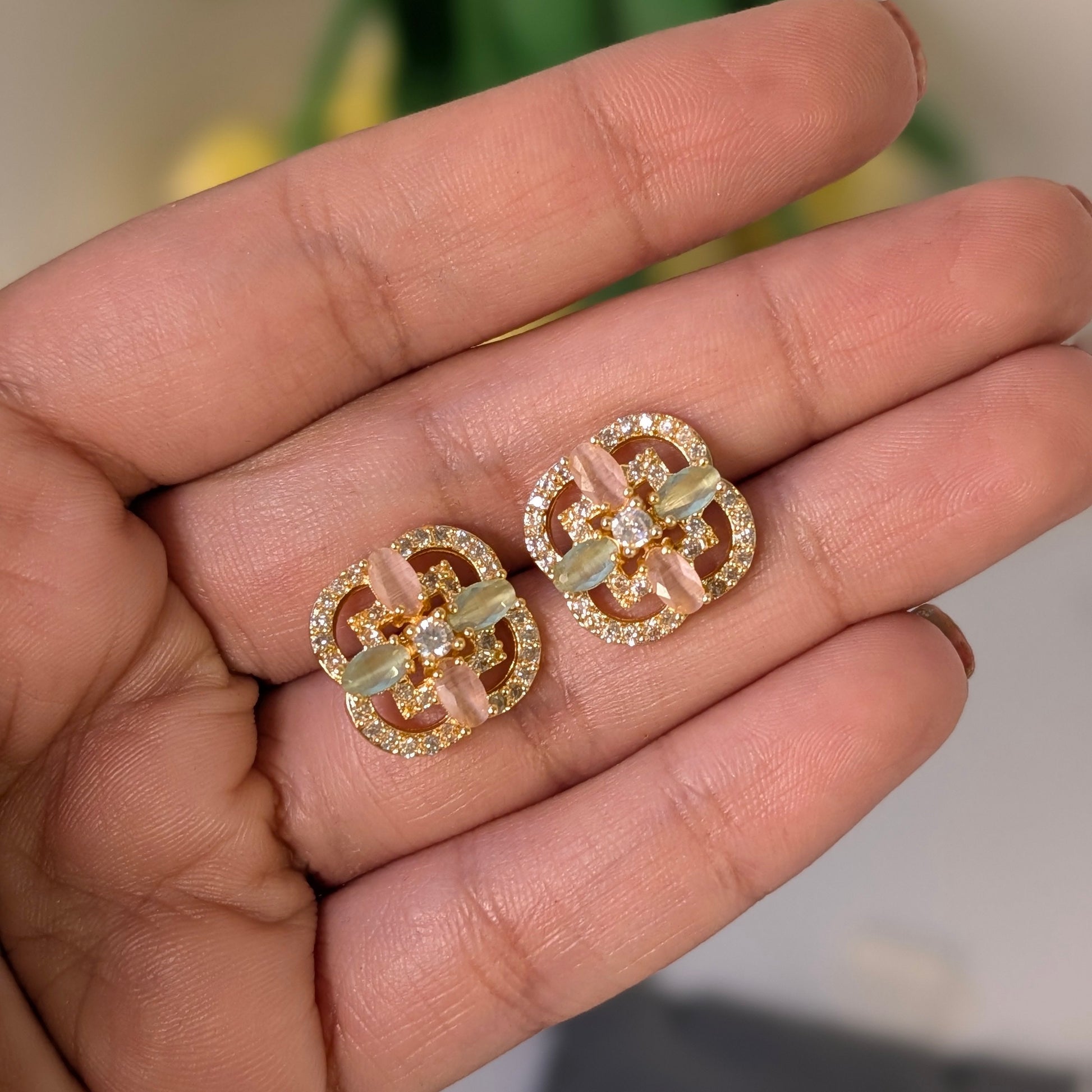 Gold and diamond earrings held in a hand with a blurred natural background