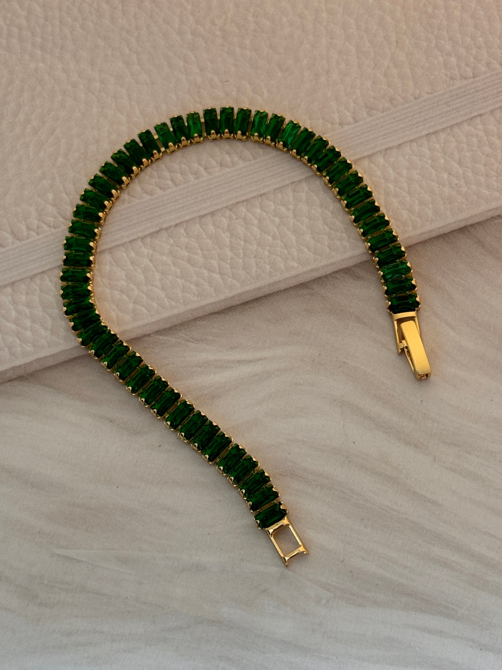 Green gemstone bracelet with gold clasp on a textured beige surface