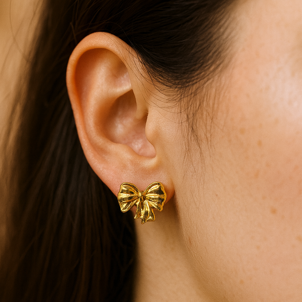 Gold bow-shaped earrings worn by a person with dark hair.