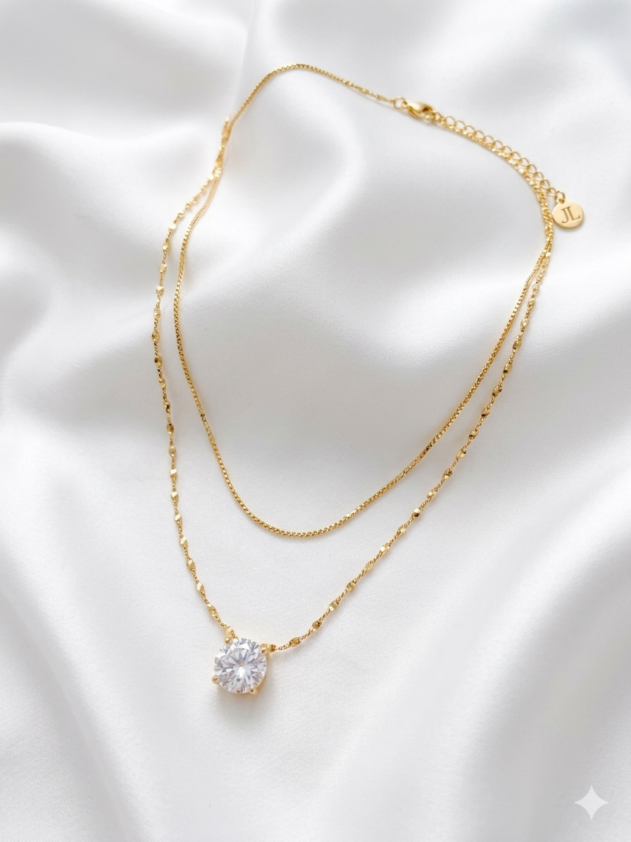 Gold necklace with a clear gemstone on a white fabric background