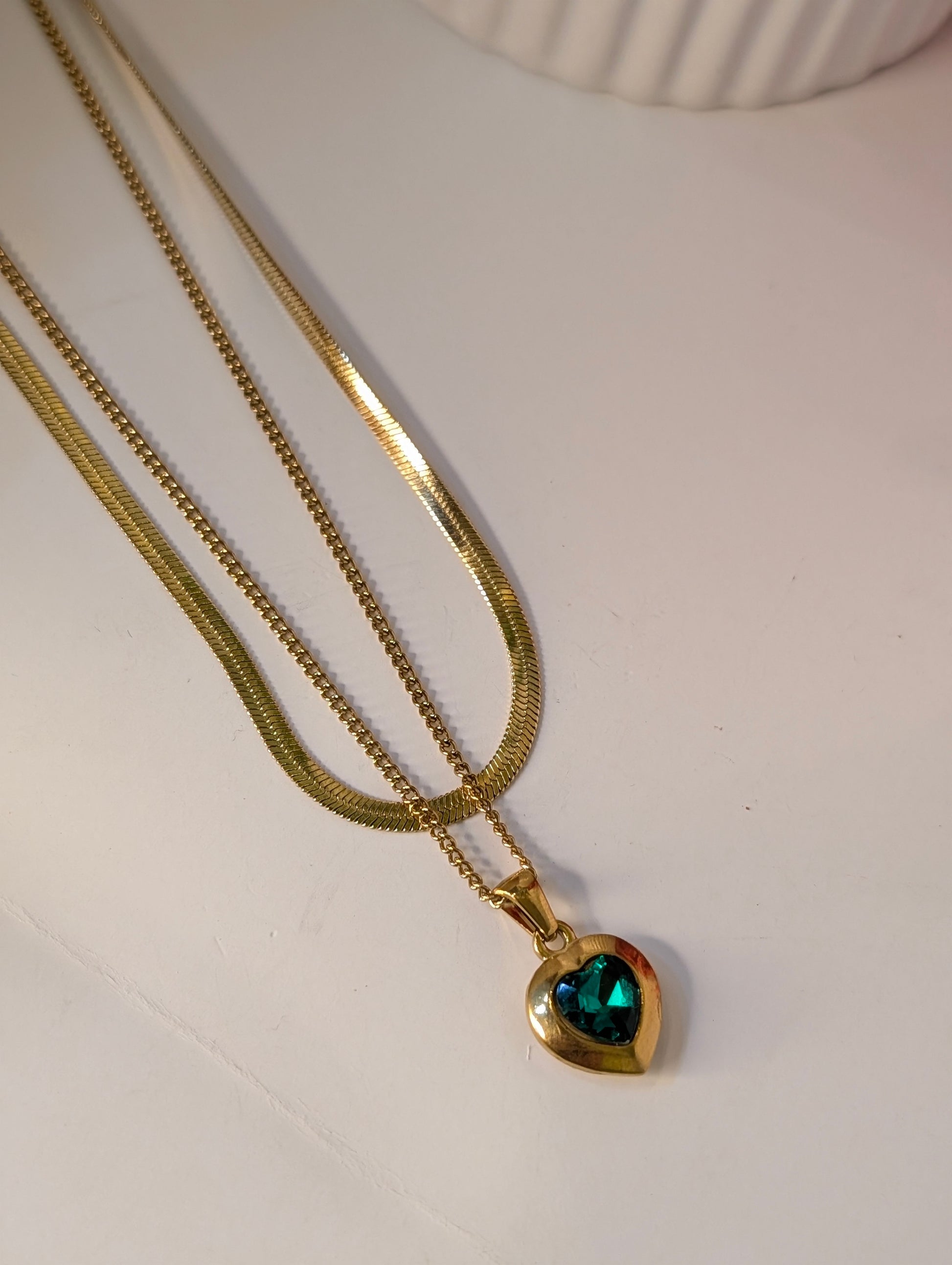 Gold necklace with a heart-shaped pendant on a white surface
