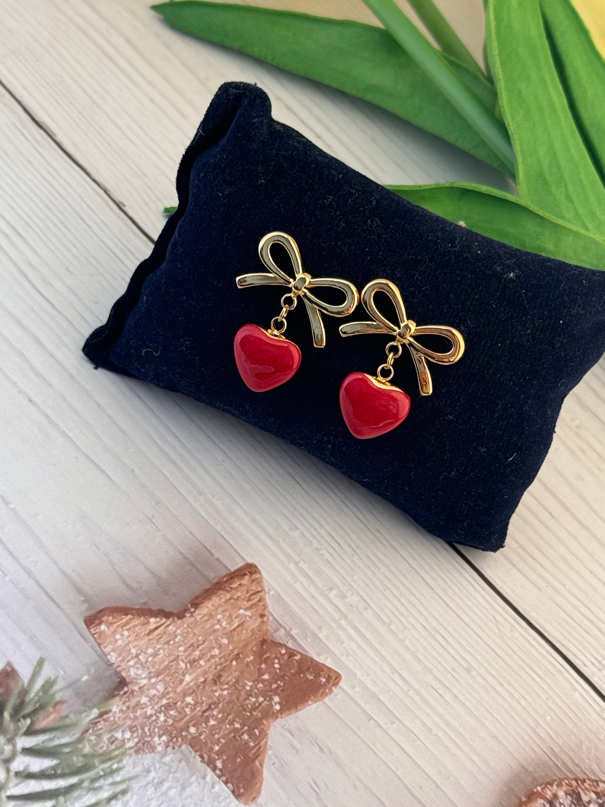Gold bow and red heart earrings on a black velvet cushion with decorative elements.