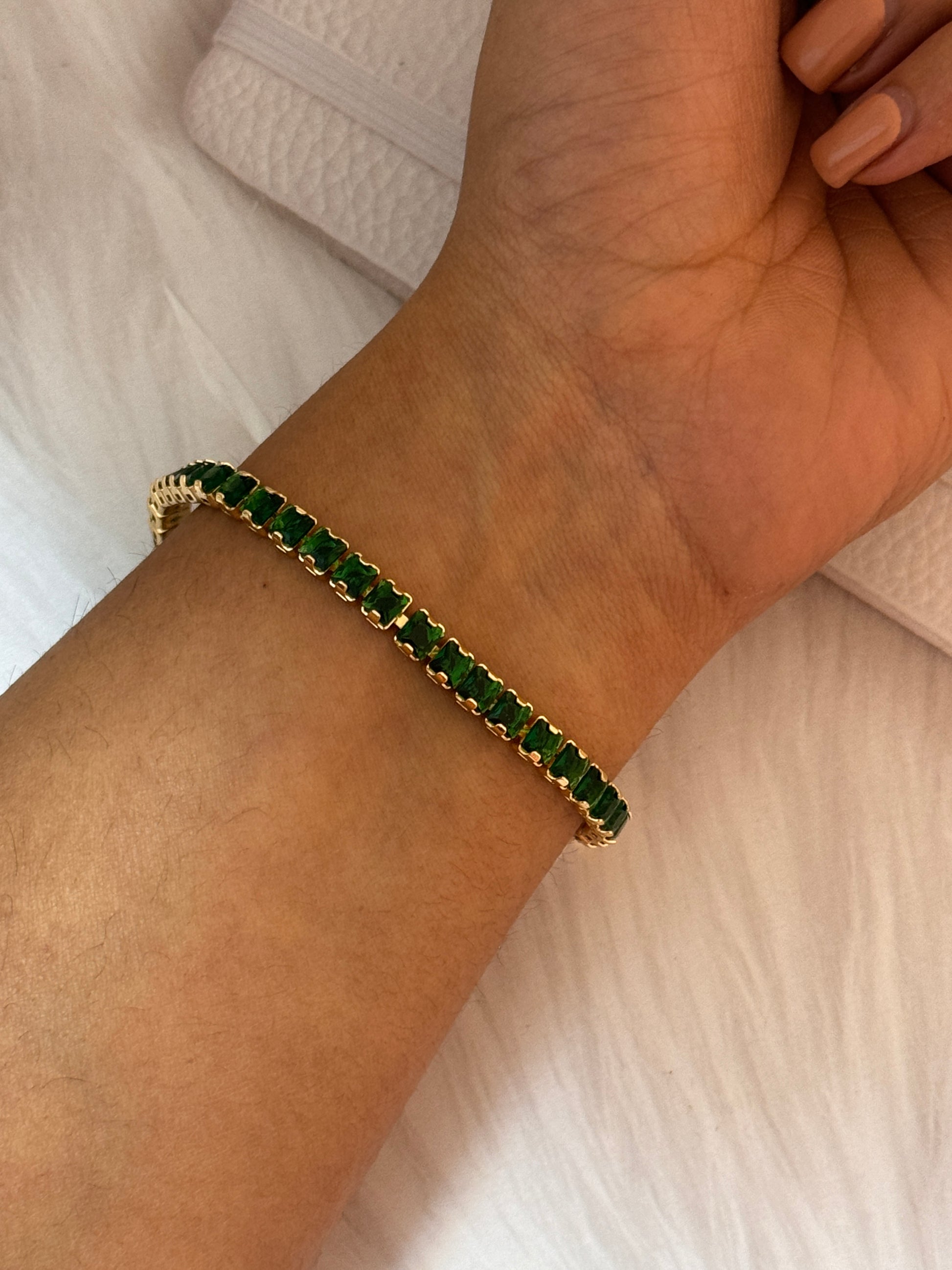 Gold bracelet with green stones on a wrist against a light background