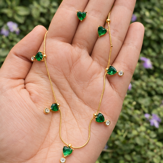 Gold necklace with green gemstones held in a hand against a blurred green background