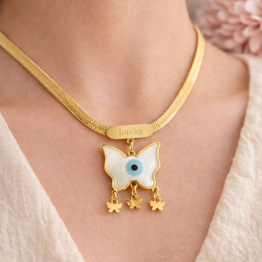 Gold necklace with a butterfly pendant featuring an eye design, worn by a person.