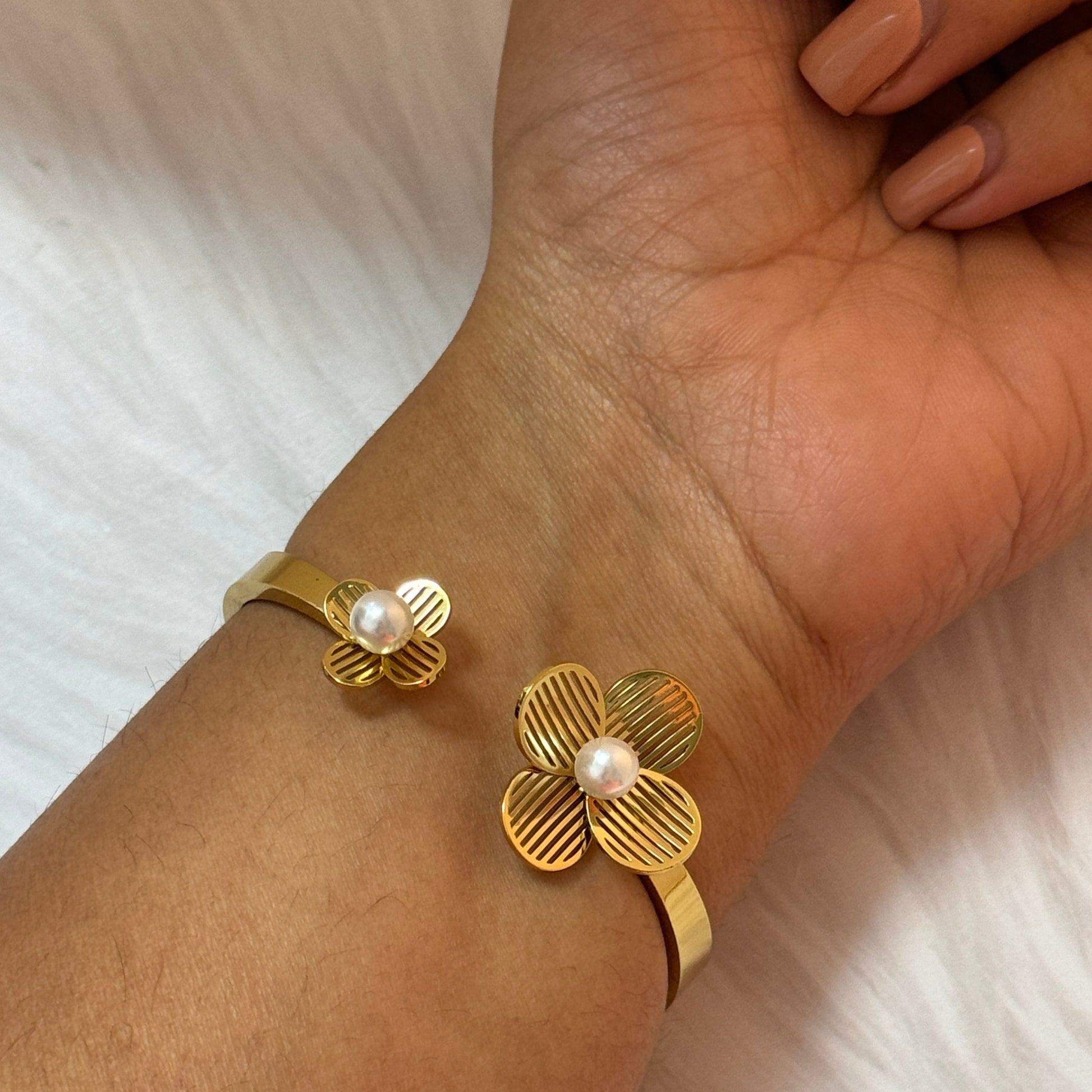 Gold floral bracelet with pearl center on a wrist against a white background