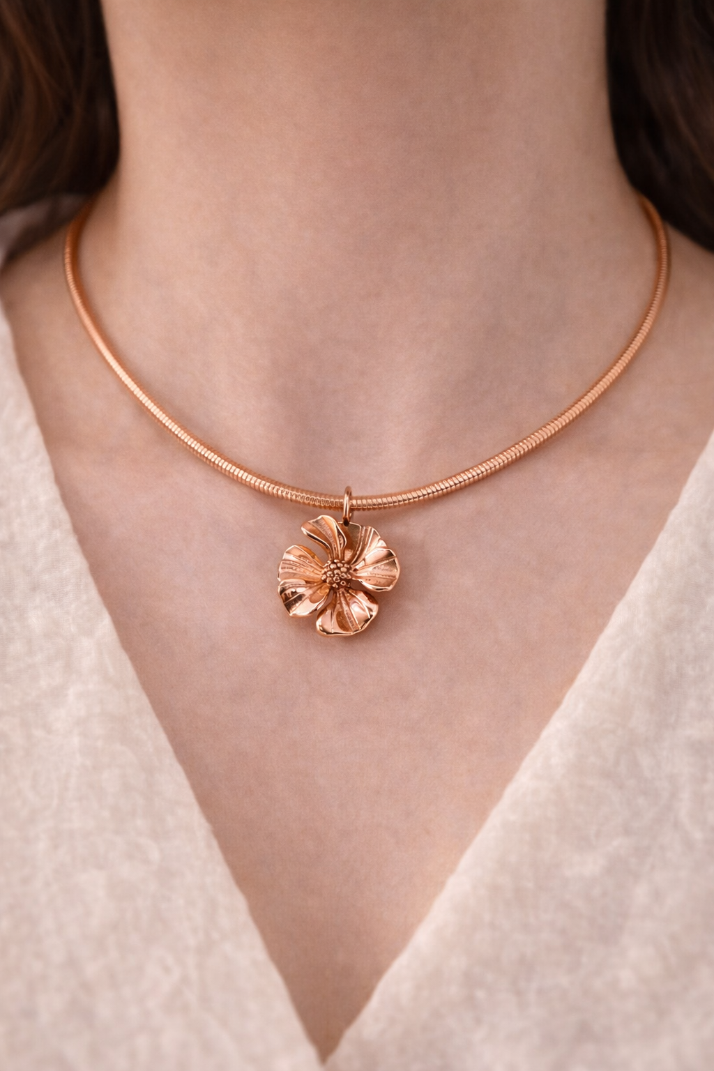 Rose gold necklace with a floral pendant on a person wearing a white top.