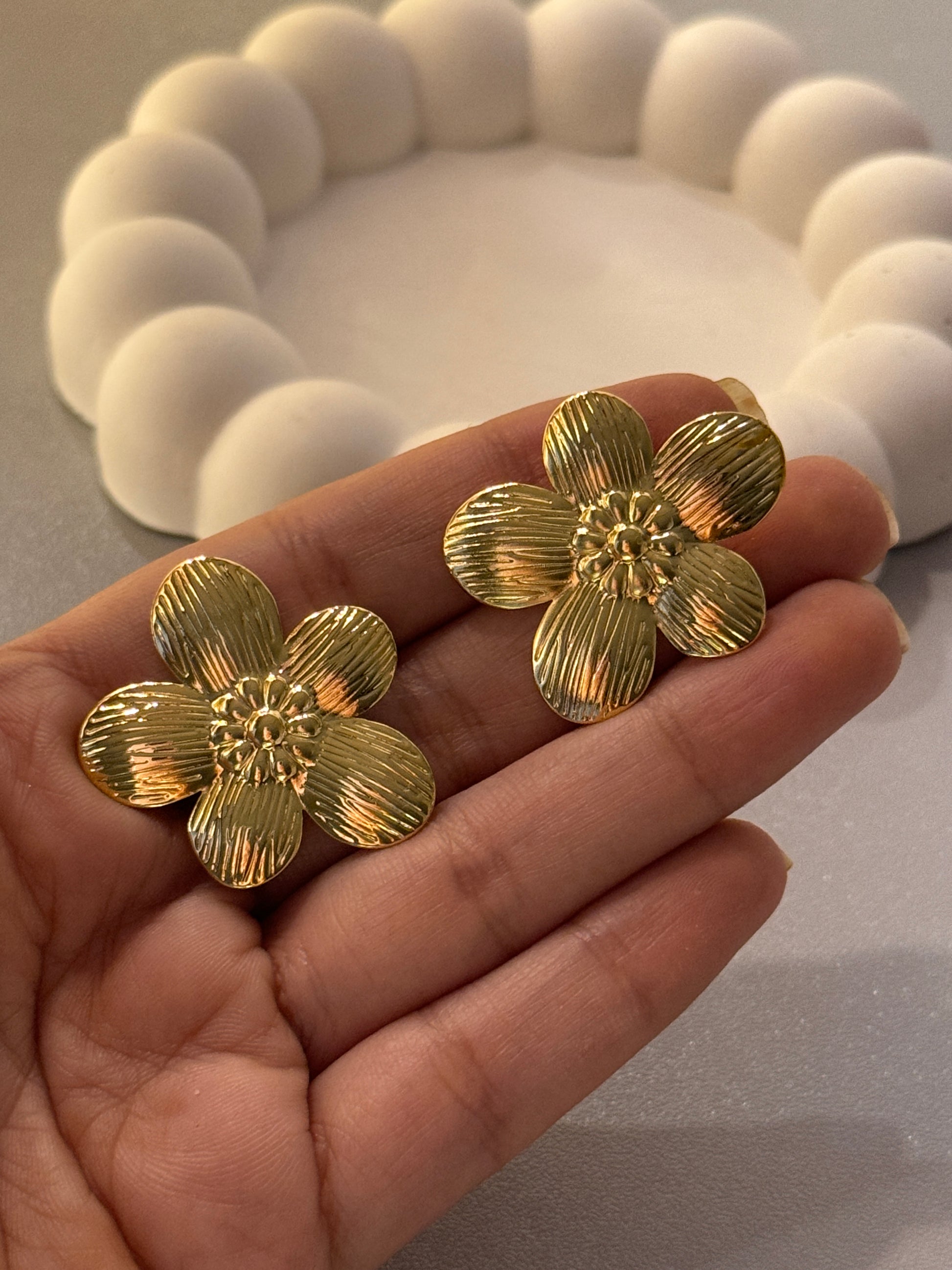 Gold flower-shaped earrings held in a hand with a blurred background