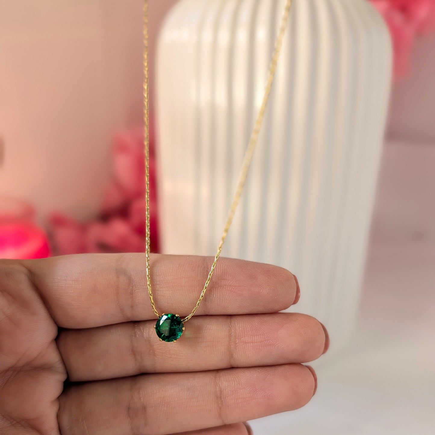 Gold necklace with a green gemstone held by a hand against a blurred background