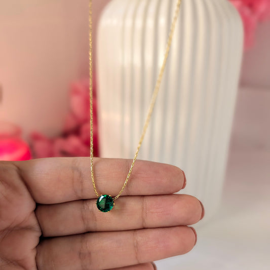 Gold necklace with a green gemstone held by a hand against a blurred background