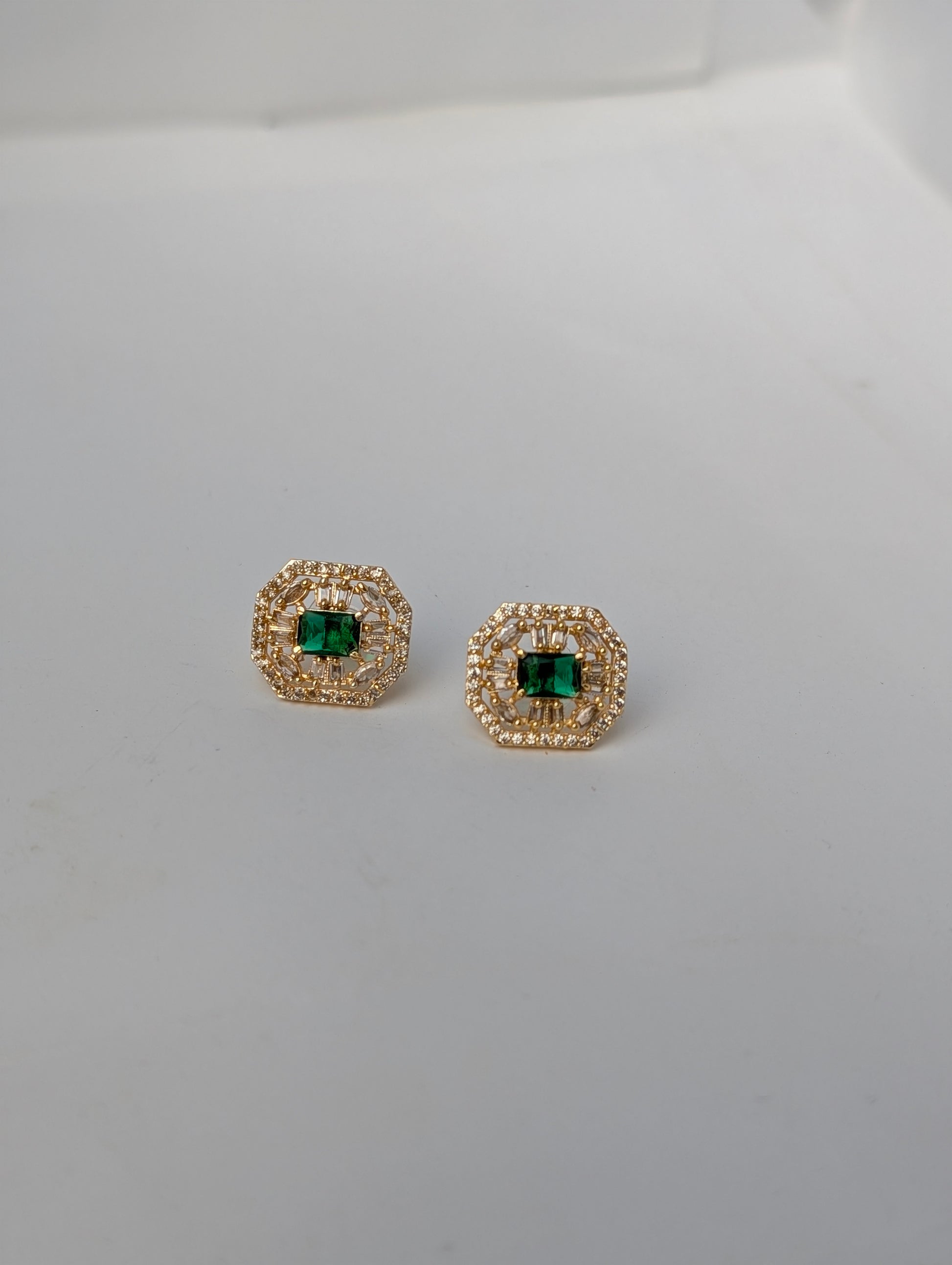 Pair of gold earrings with green gemstones on a light gray background