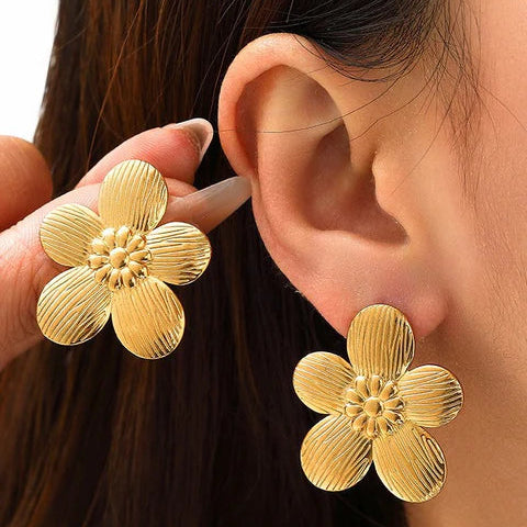 Gold flower earrings being worn and held up to an ear.