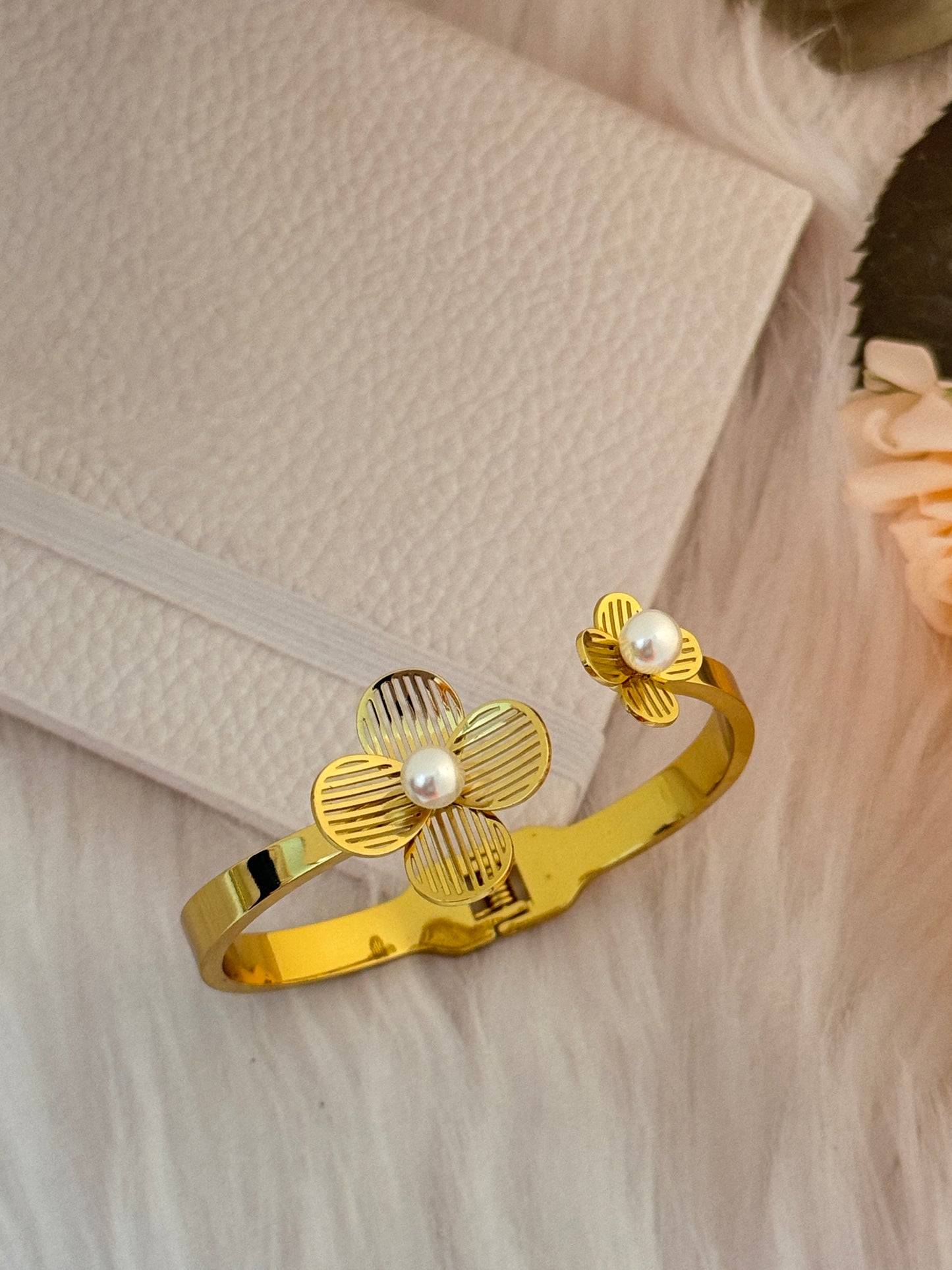 Gold bracelet with floral design and pearls on a textured surface