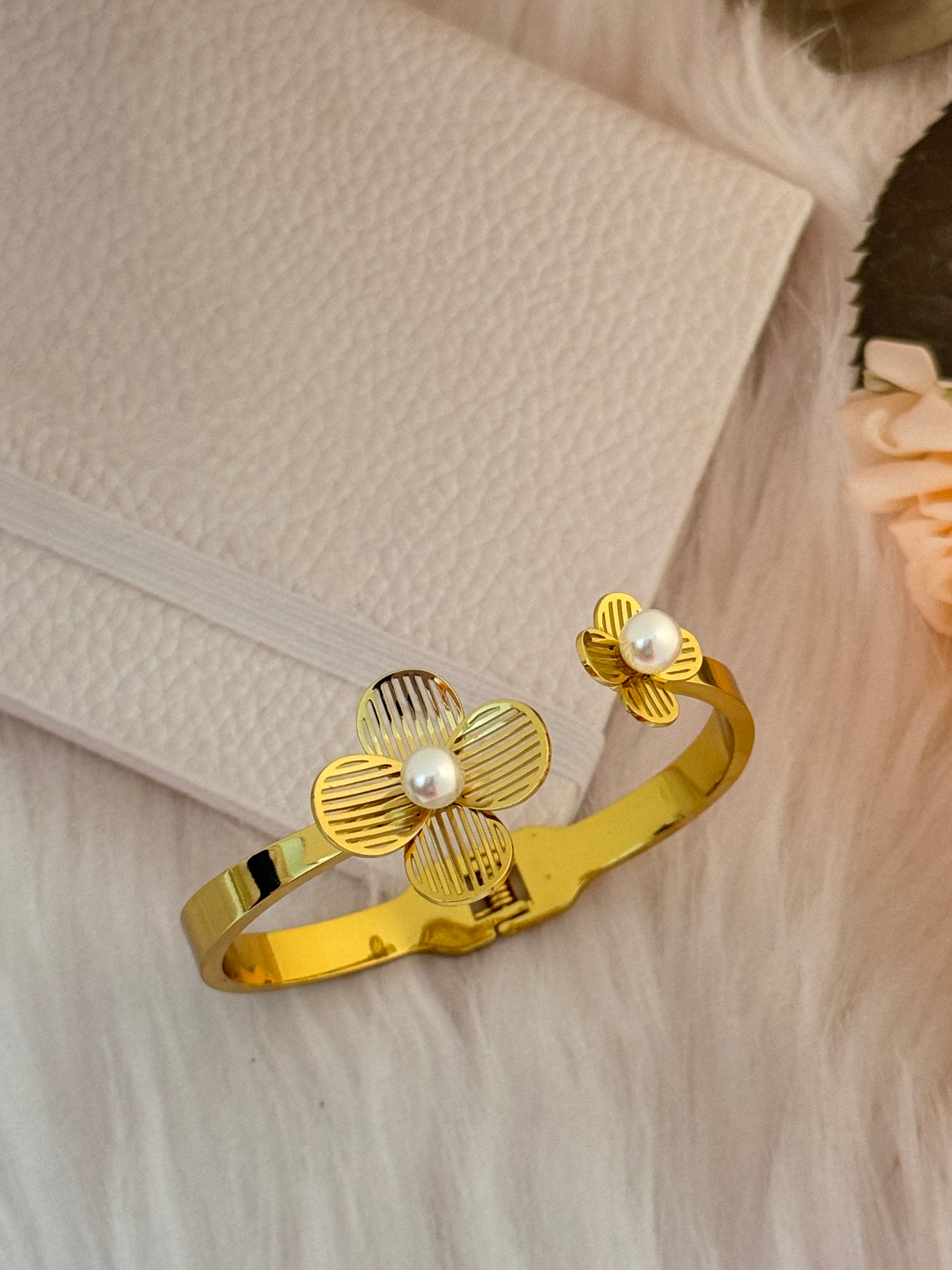 Gold bracelet with floral design and pearls on a textured surface