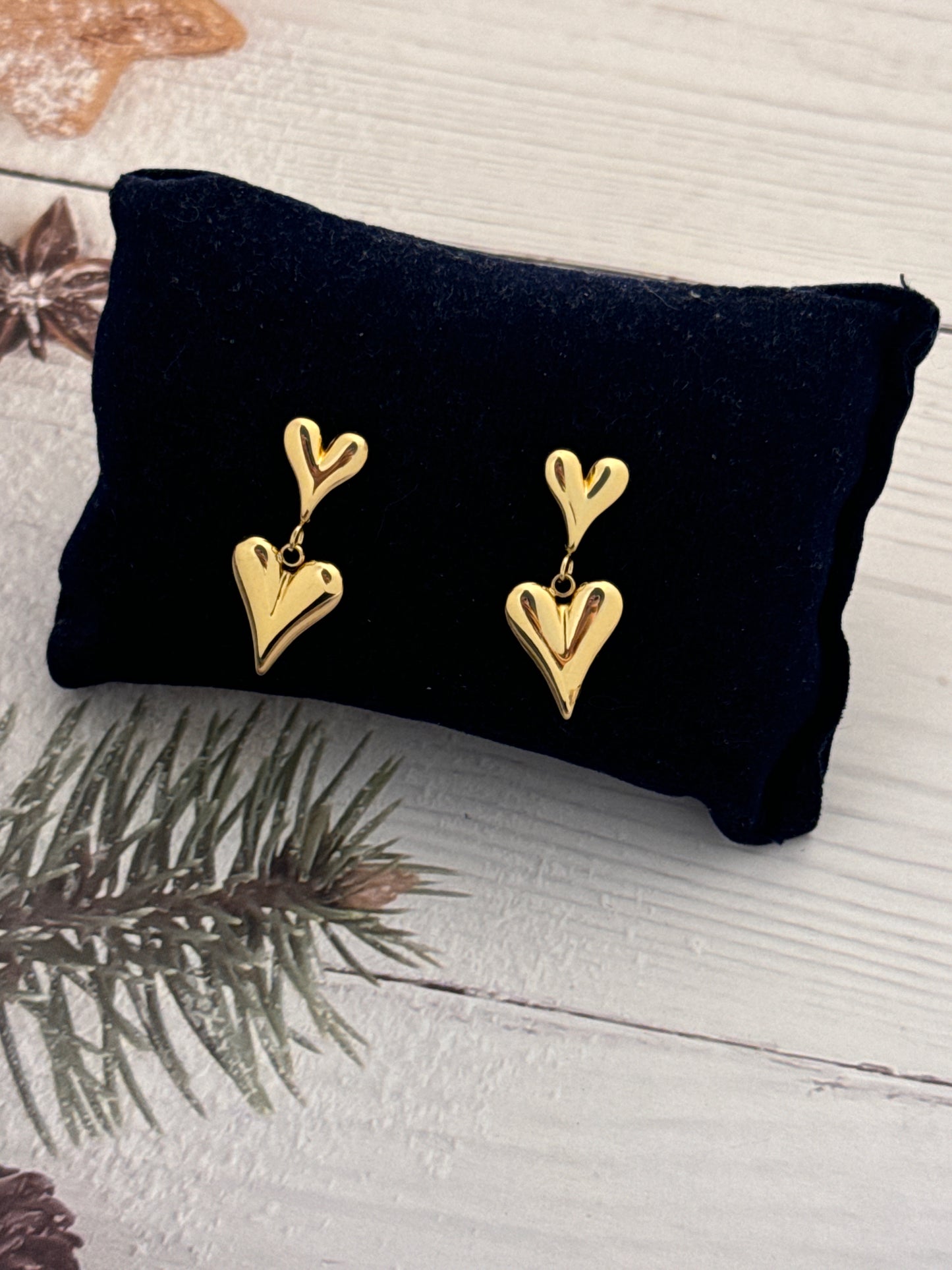 Gold heart-shaped earrings on a black pillow with a wooden background