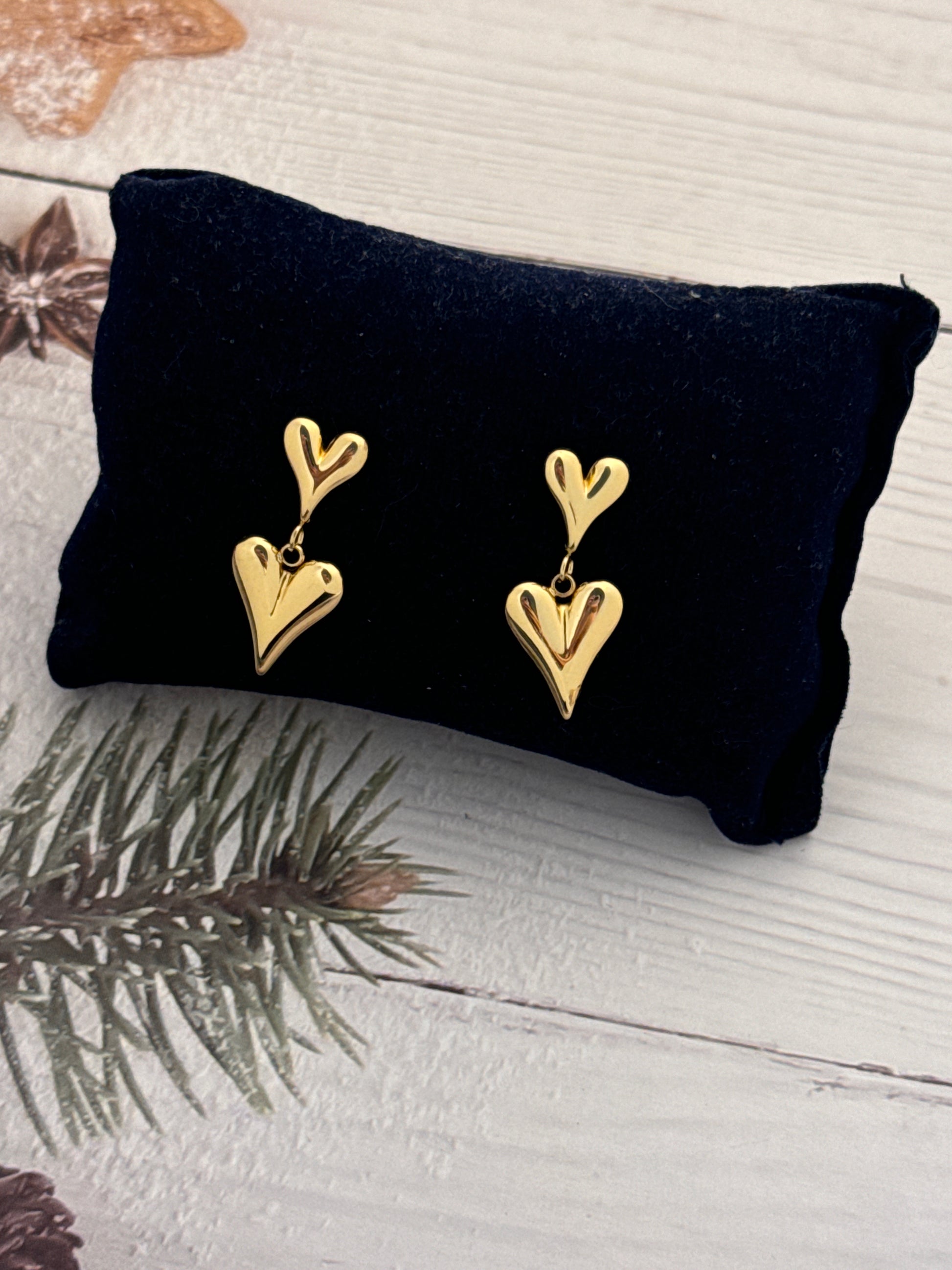 Gold heart-shaped earrings on a black pillow with a wooden background