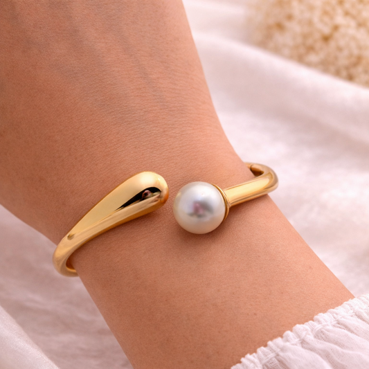 Gold bracelet with a pearl on a wrist against a soft fabric background