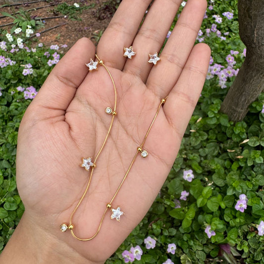 Gold necklace with star-shaped pendants held in a hand against a floral background