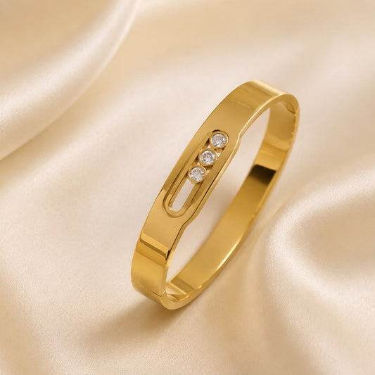A polished yellow gold ring with a small three-stone diamond accent, displayed on a draped cream satin fabric background.
