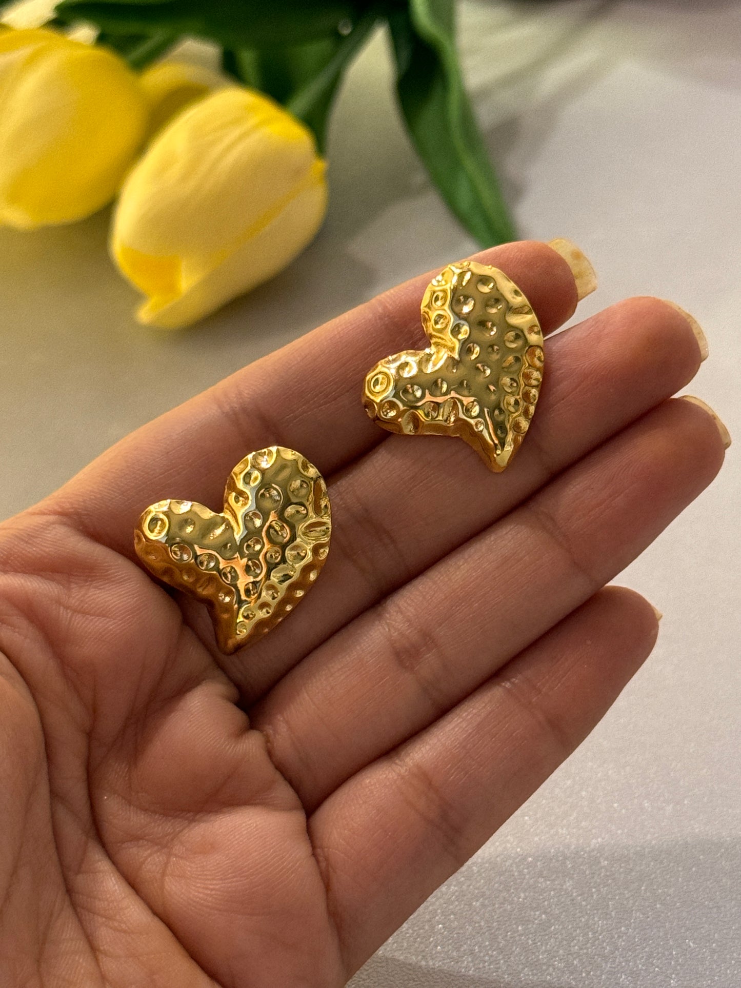 Gold earrings shaped like continent outlines held in a hand with yellow tulips in the background