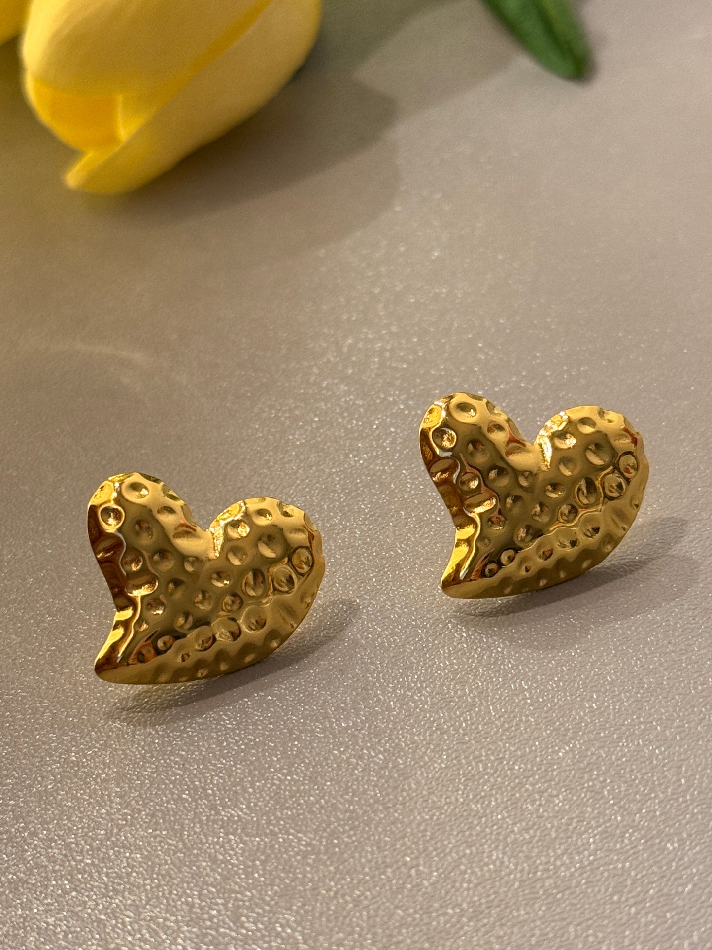Gold heart-shaped earrings on a gray surface with a yellow tulip.