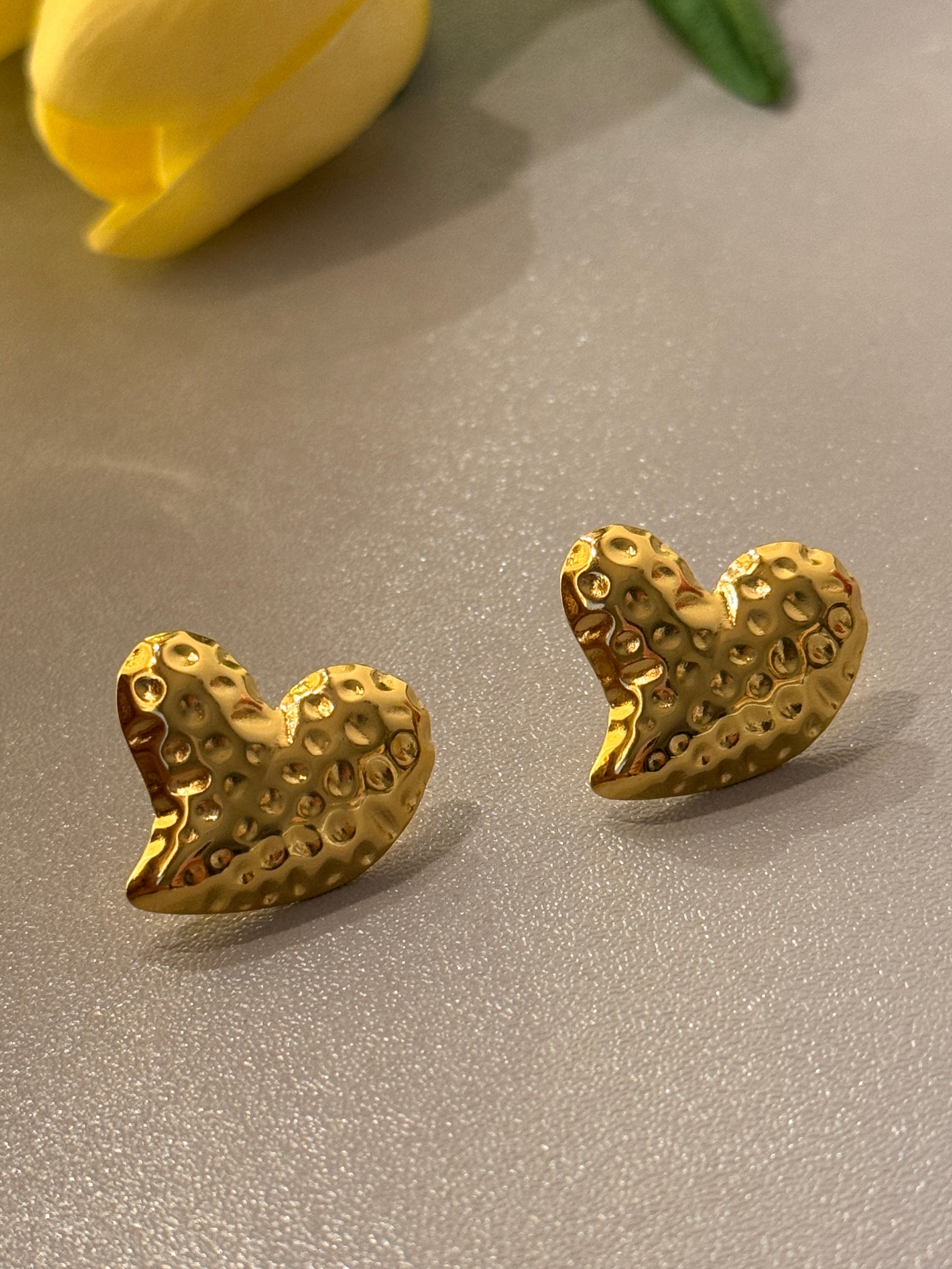 Gold heart-shaped earrings on a gray surface with a yellow tulip.