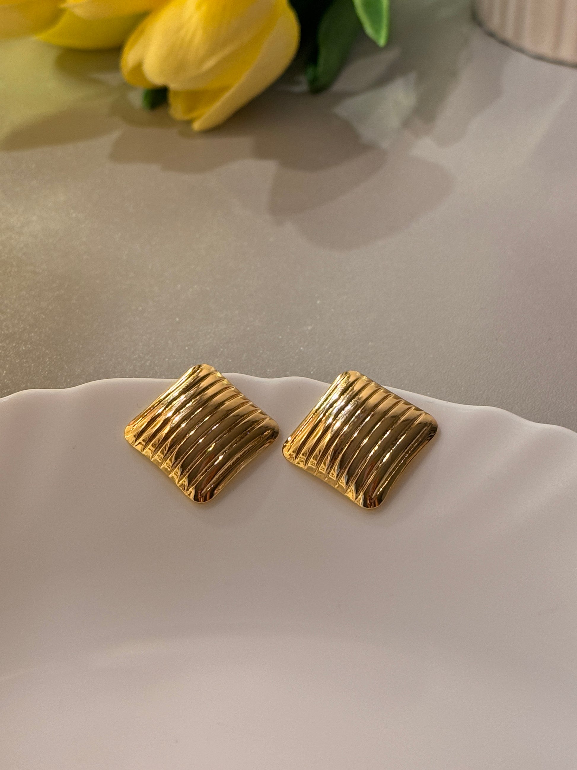 Gold square earrings on a white surface with a blurred background