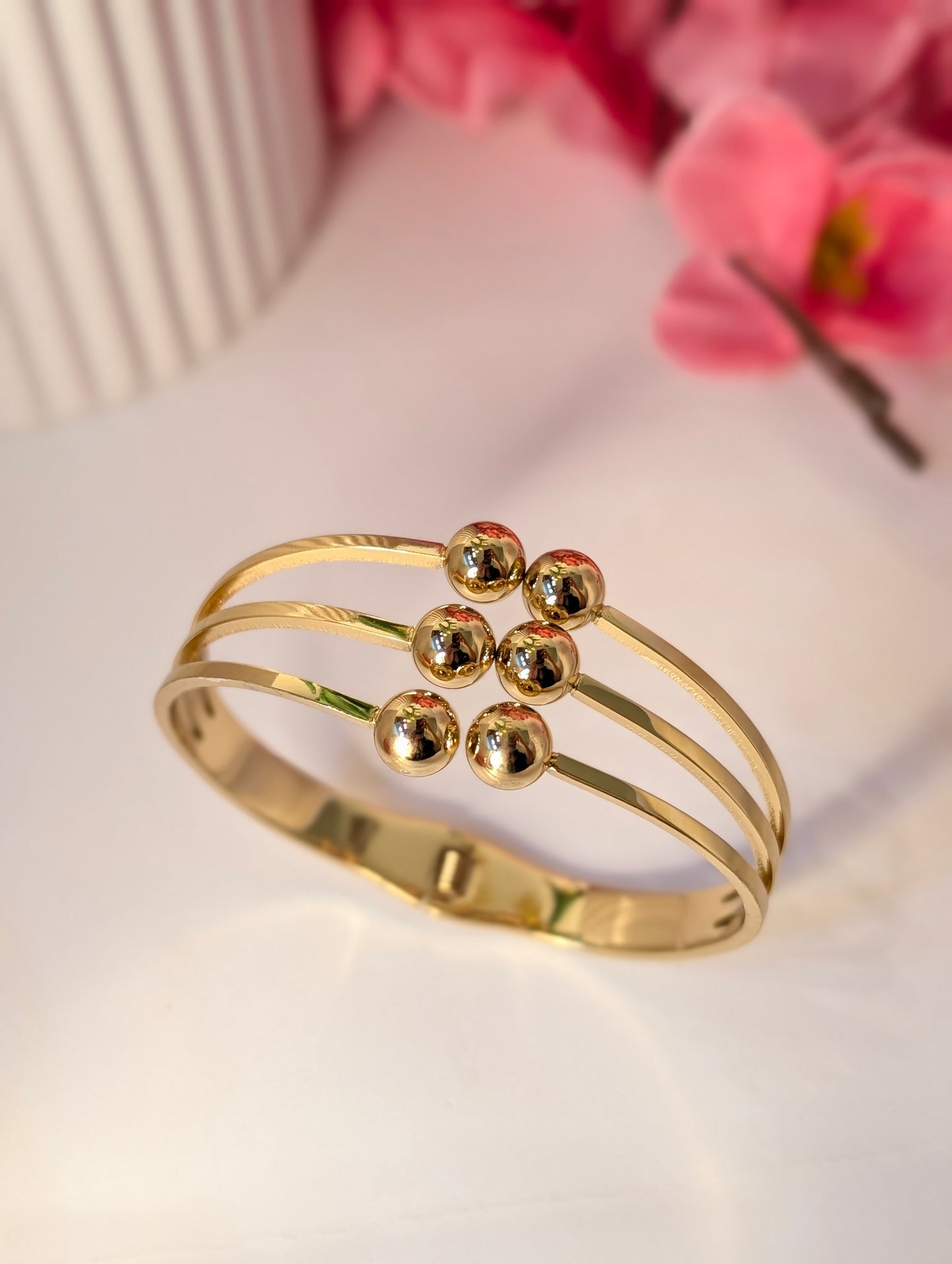 Gold bracelet with three spherical charms on a light background