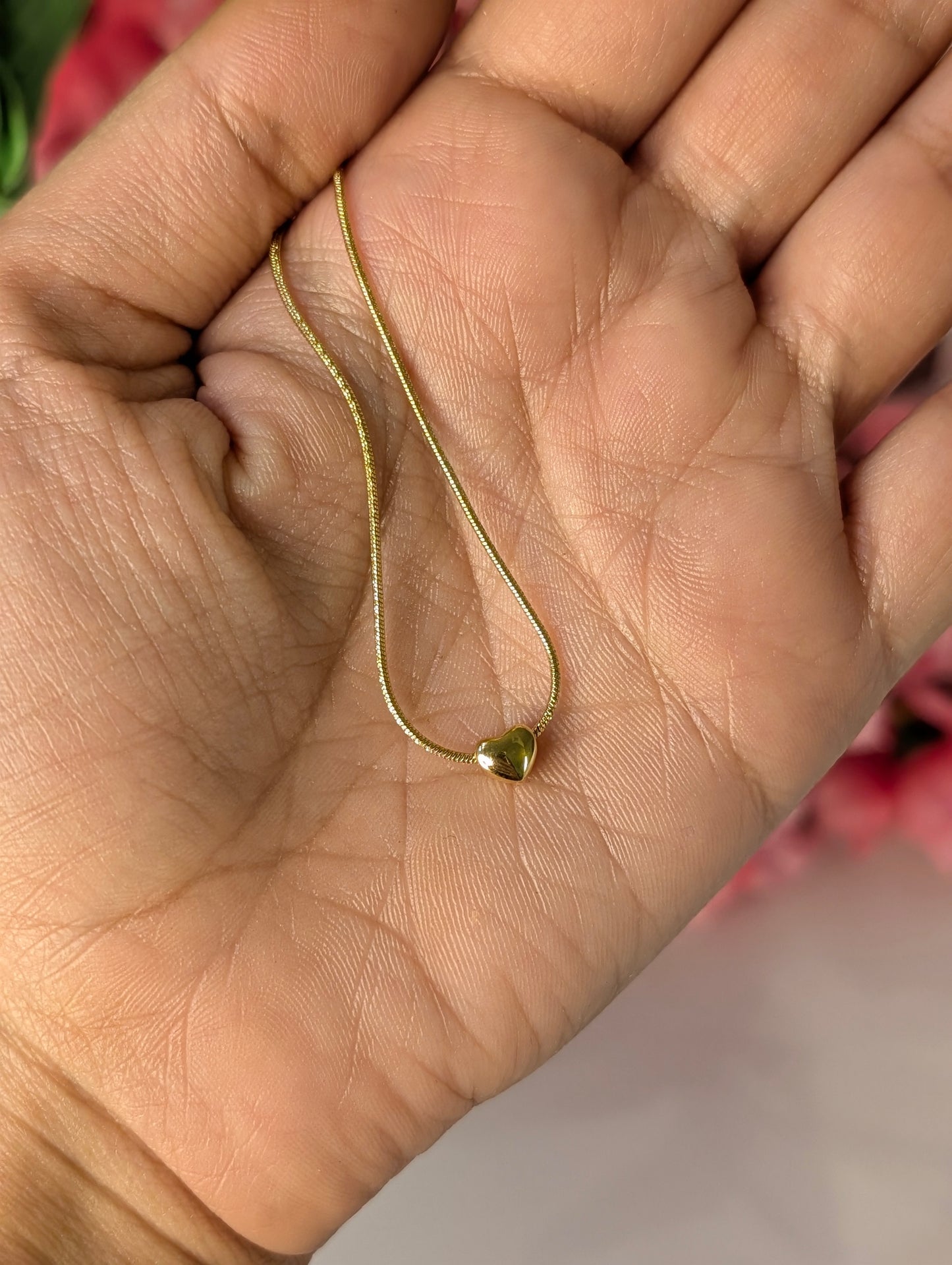 Gold chain with heart detail held in a hand