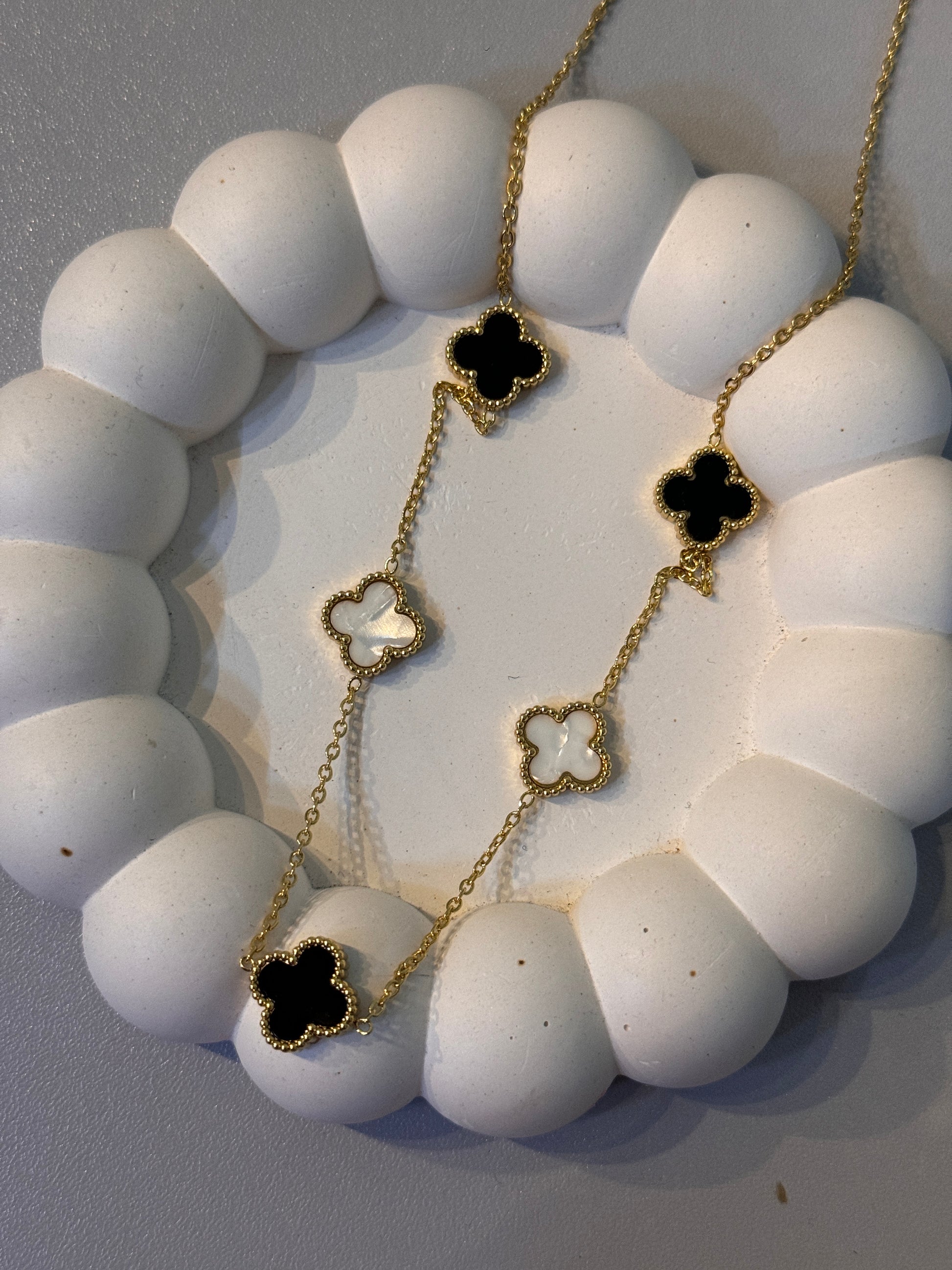 Gold necklace with black clover-shaped pendants on a white stone surface