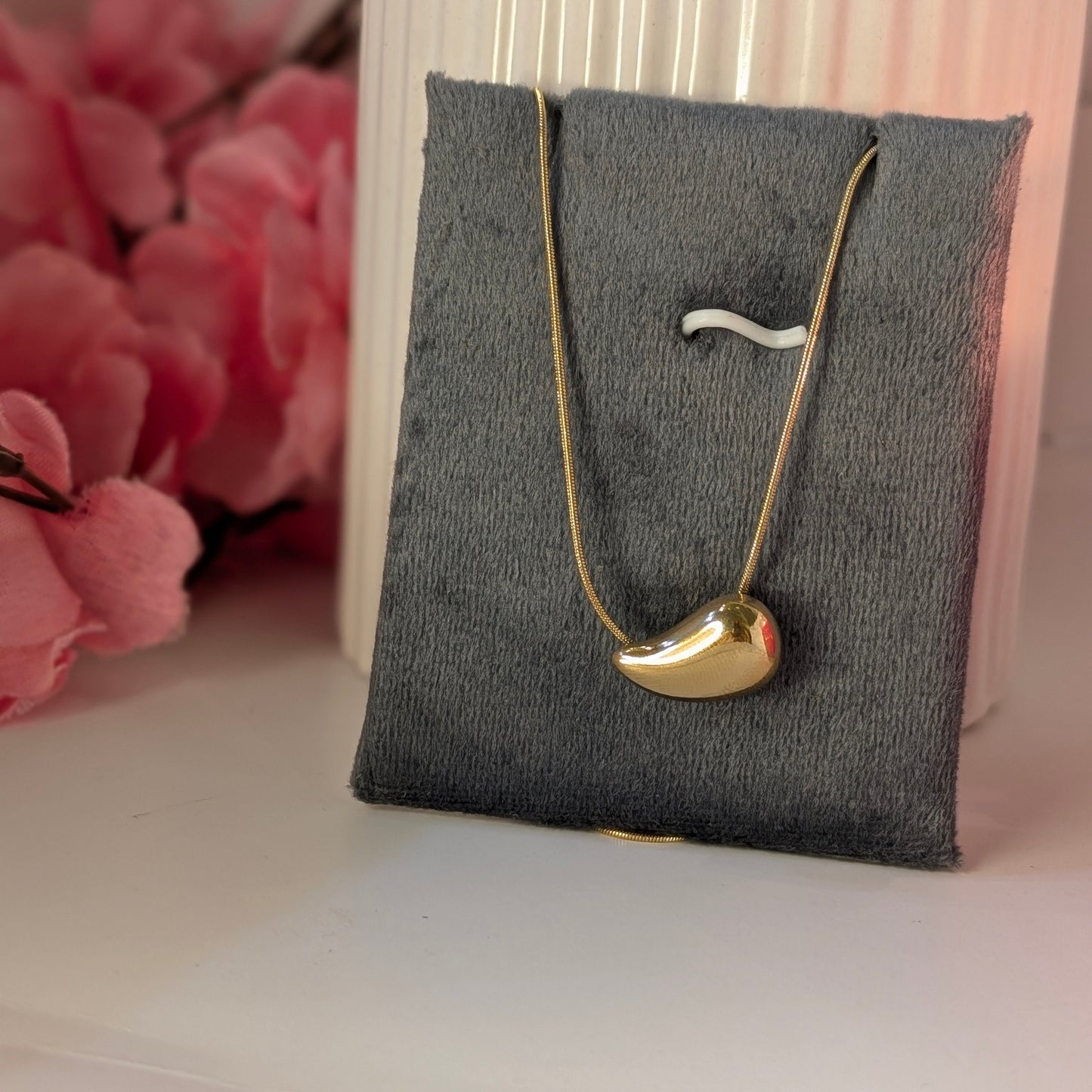 Gold necklace on a gray jewelry pillow with pink flowers in the background