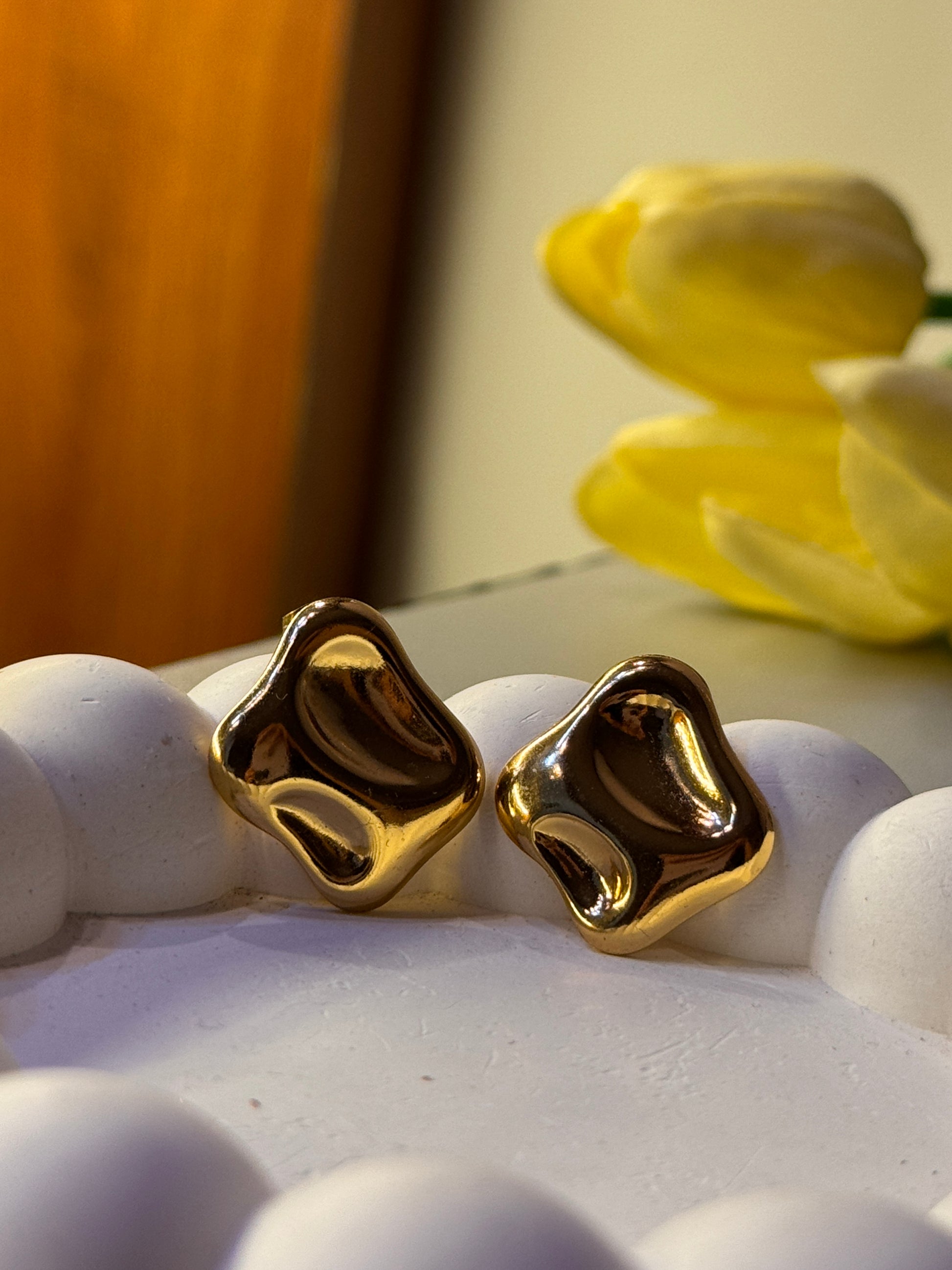 Gold grillz on a white surface with yellow flowers in the background