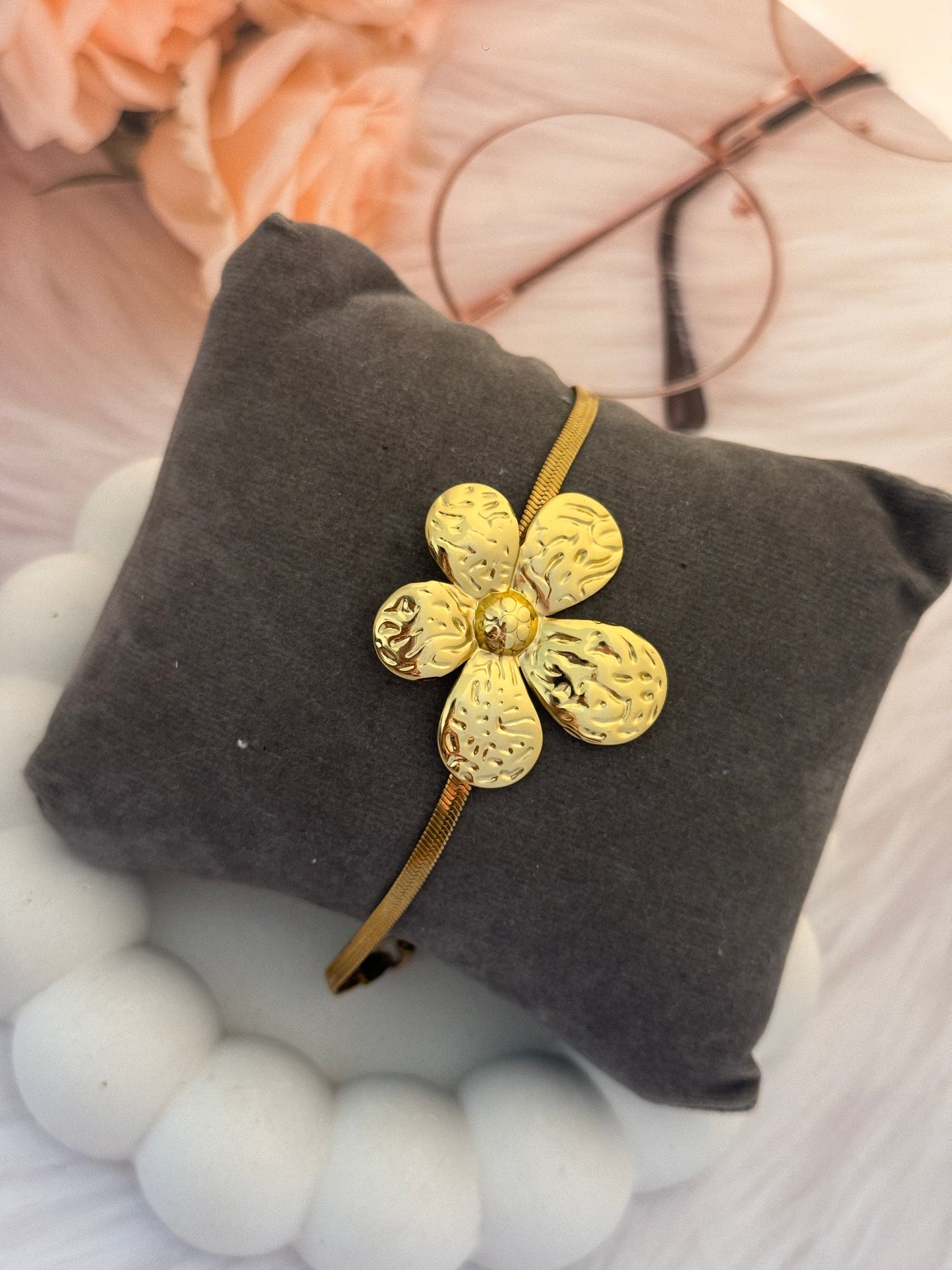 Gold flower-shaped hair clip on a gray cushion with blurred floral and fabric background