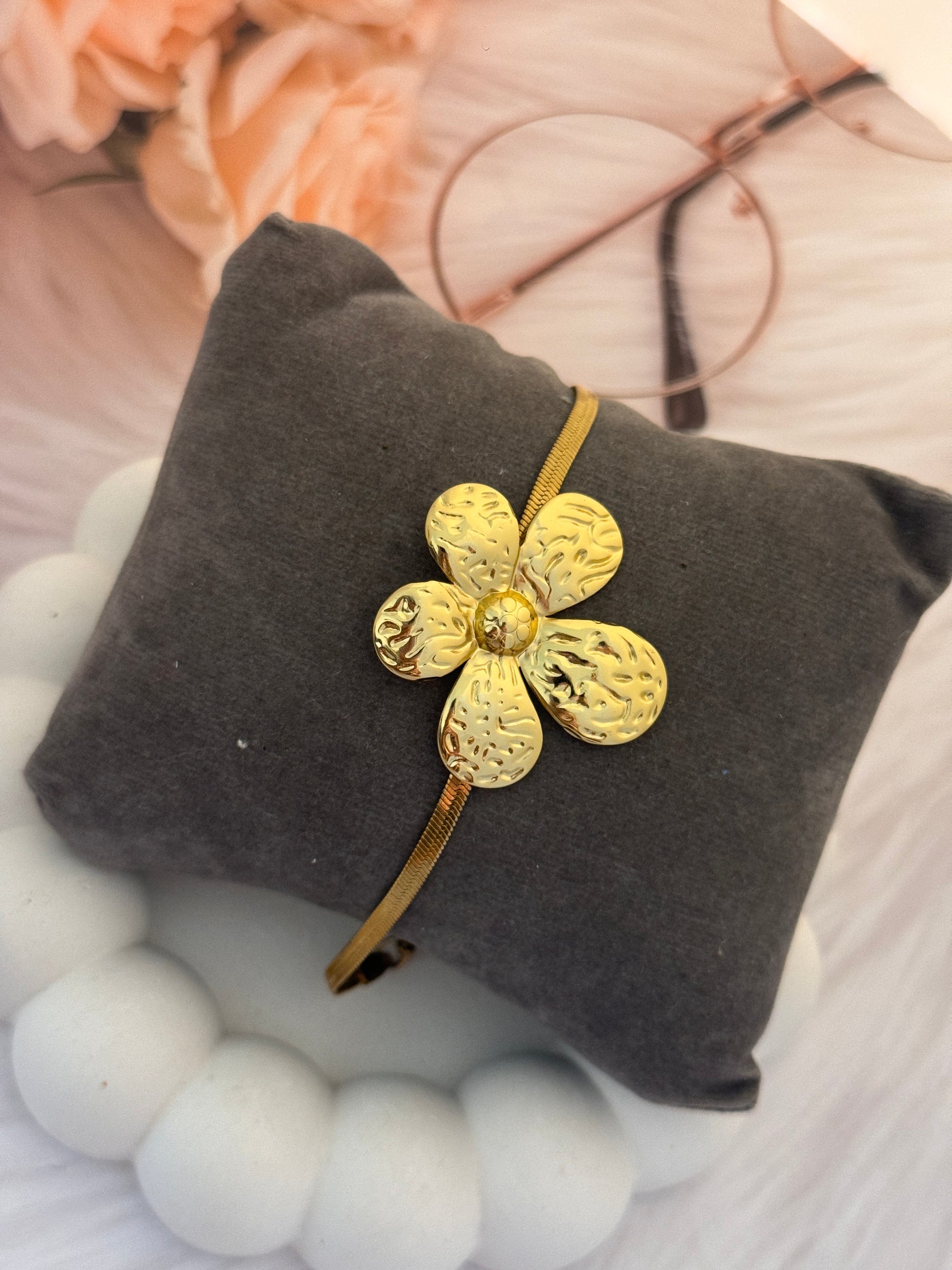 Gold flower-shaped hair clip on a gray cushion with blurred floral and fabric background