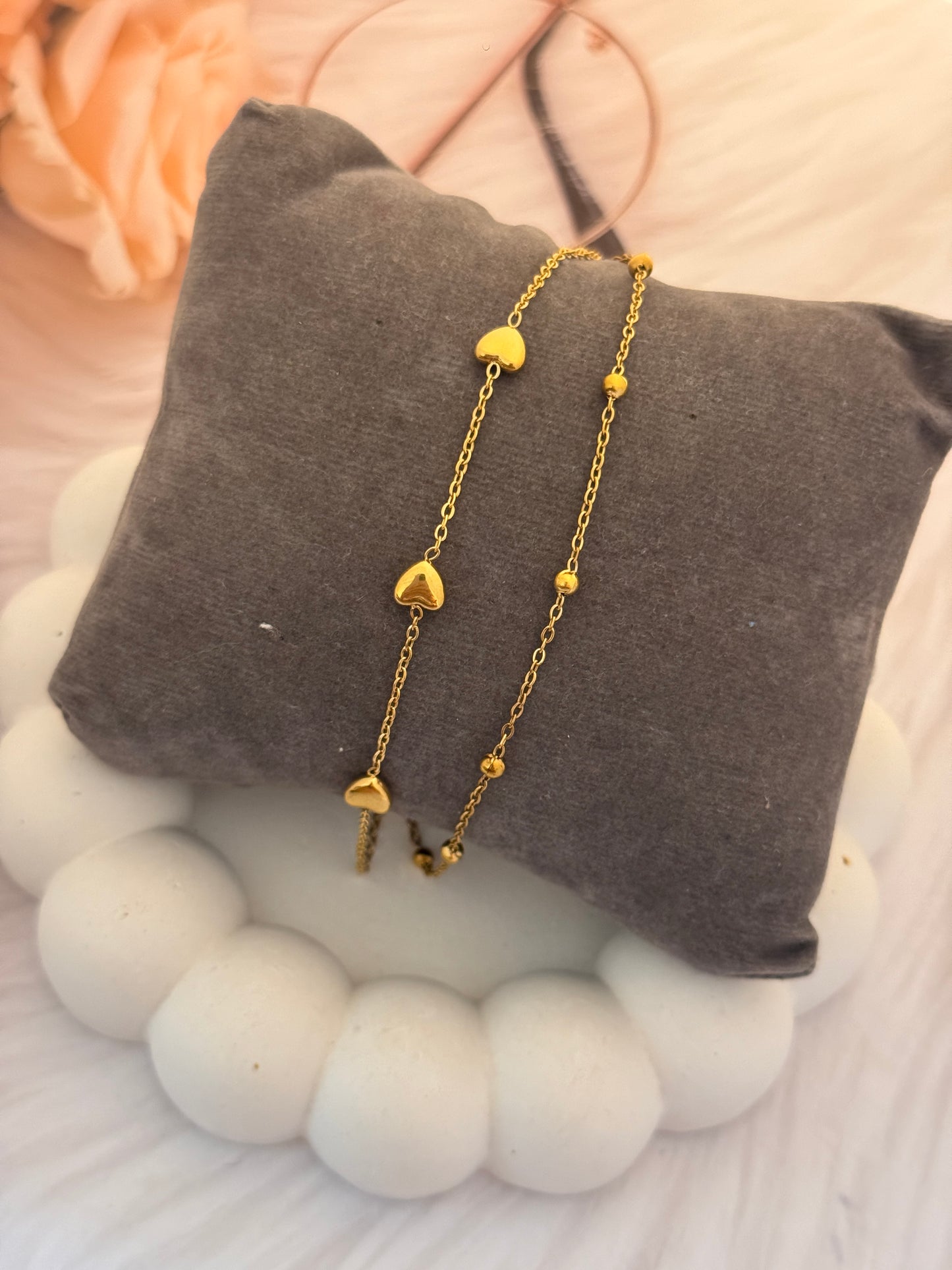 Gold heart-shaped bracelet on a gray pillow with a soft background