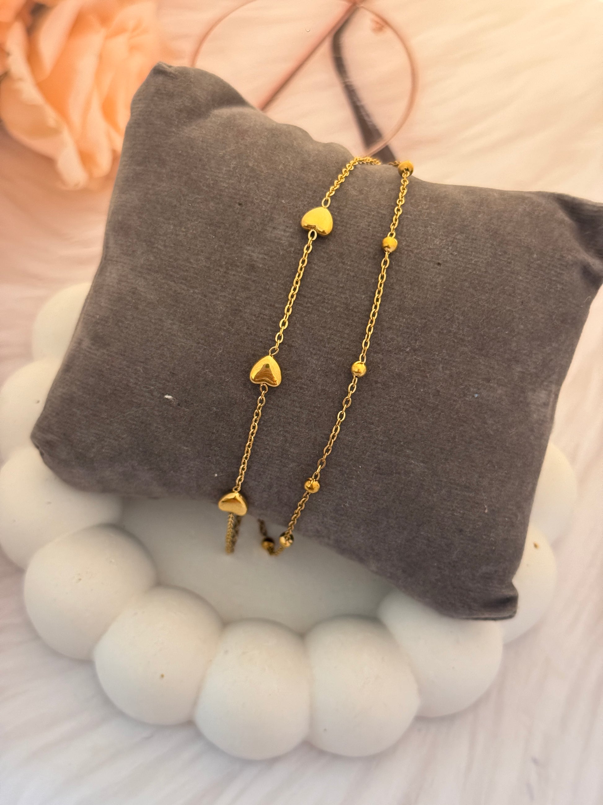 Gold heart-shaped bracelet on a gray pillow with a soft background