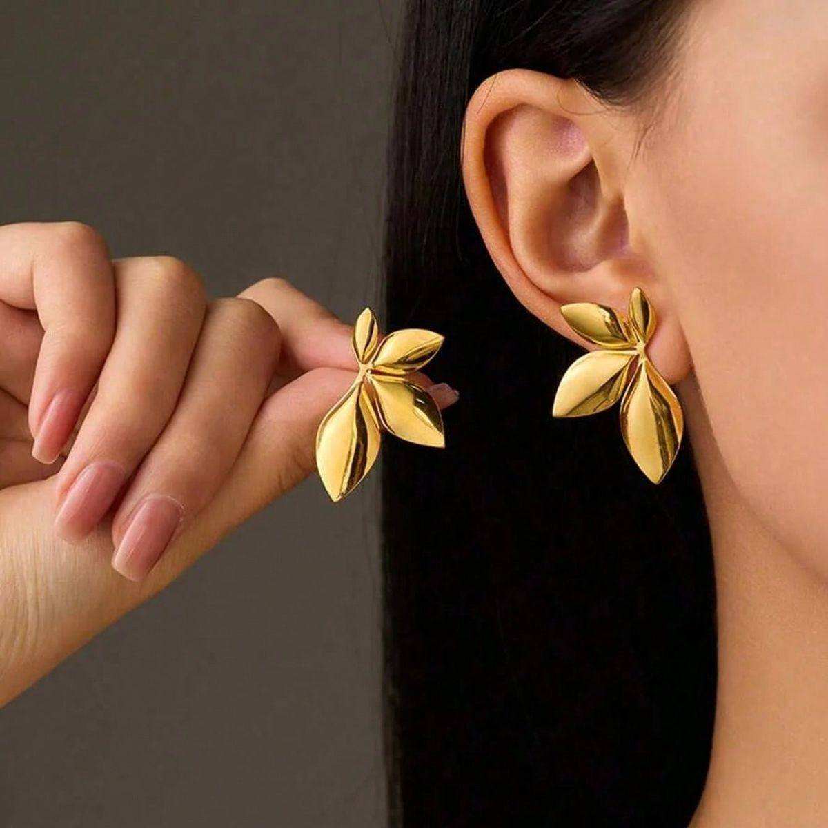 Gold leaf earrings being worn with a neutral background