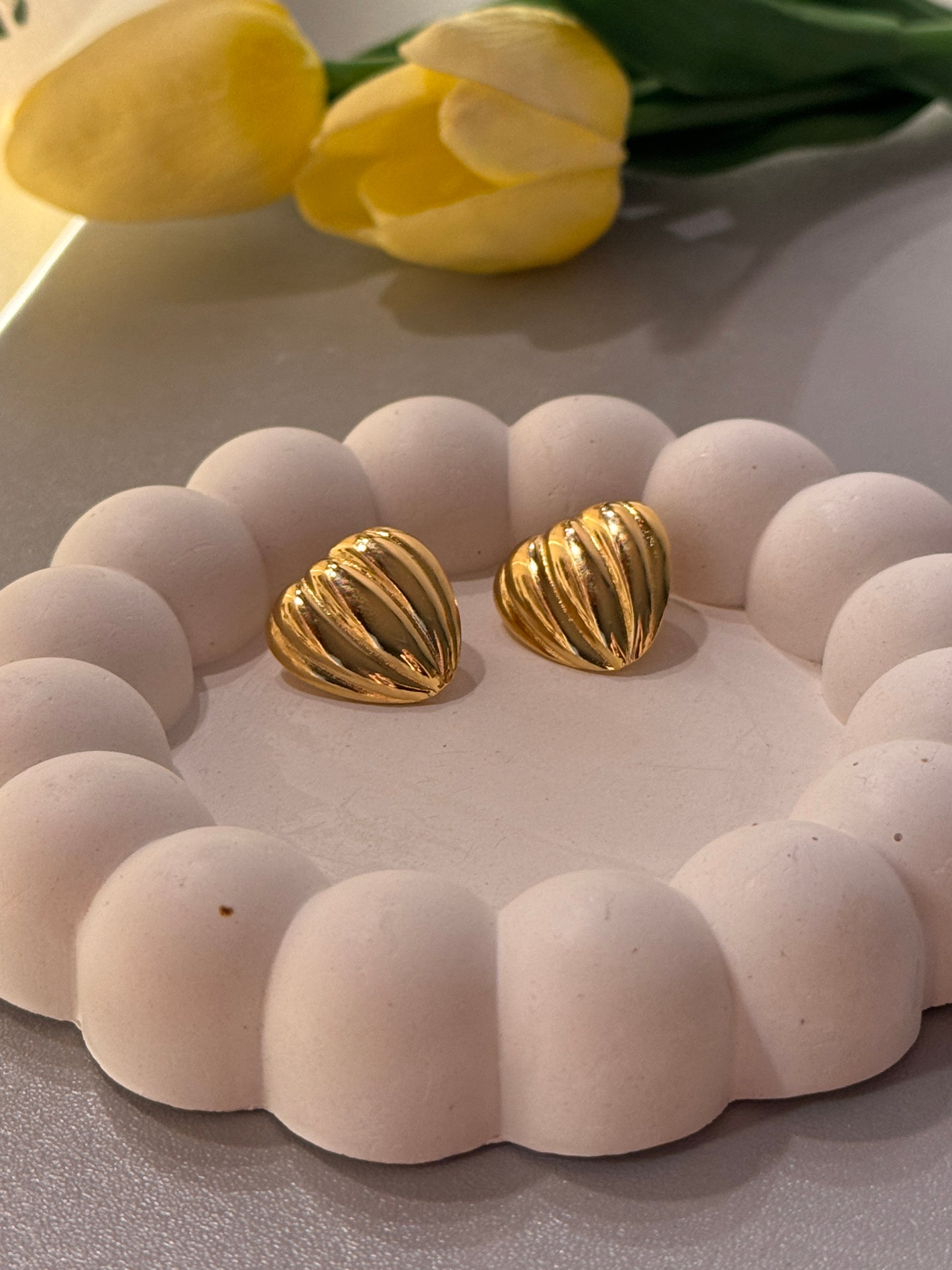 Gold textured earrings on a white textured surface with yellow tulips in the background