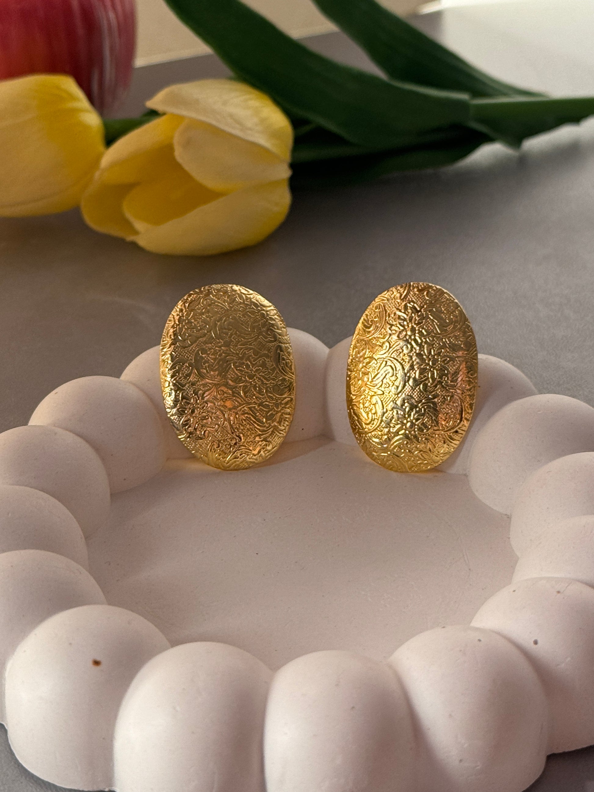 Gold earrings on a white textured surface with yellow tulips in the background