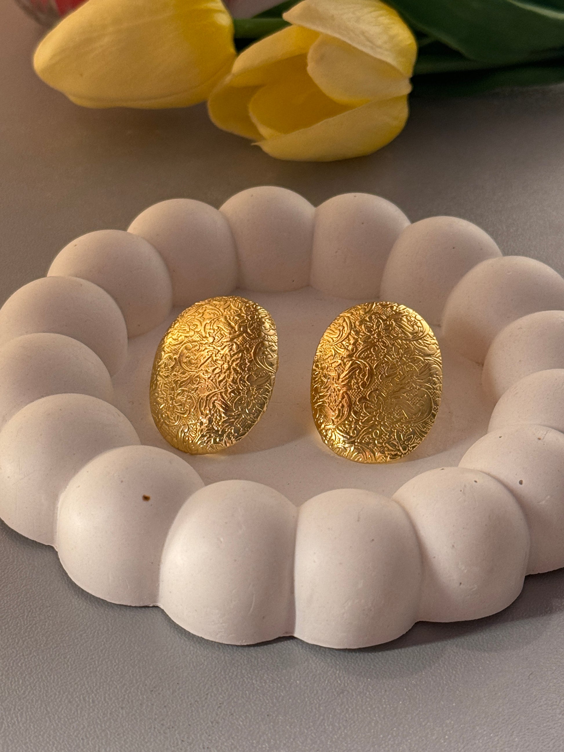 Gold earrings on a white stone surface with a yellow tulip to the left.