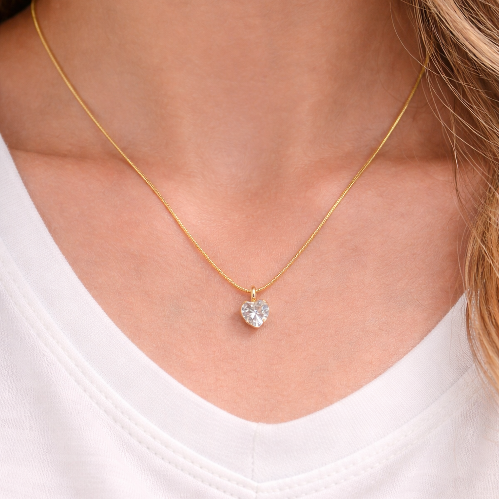 Gold necklace with a heart-shaped pendant worn by a person on a white background