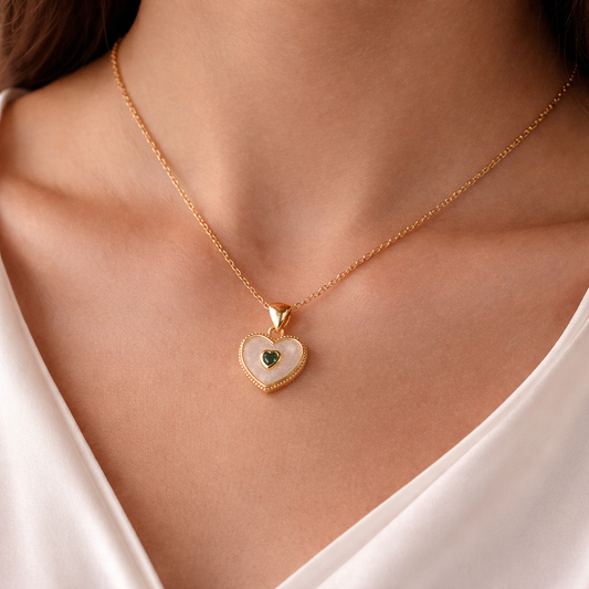 Gold heart-shaped necklace with a green gemstone on a person wearing a white top.
