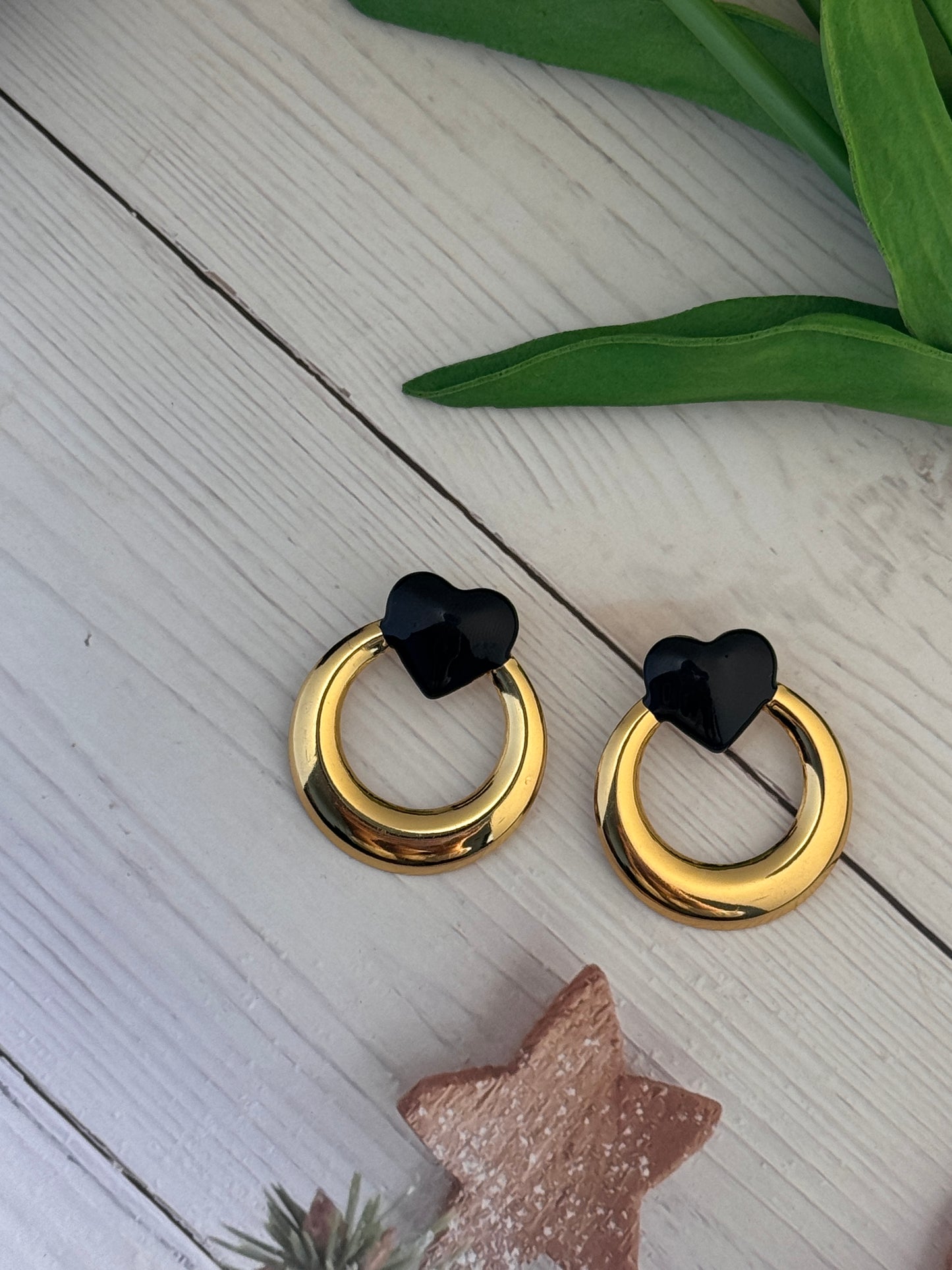 Gold hoop earrings with black heart-shaped centers on a light wooden surface.