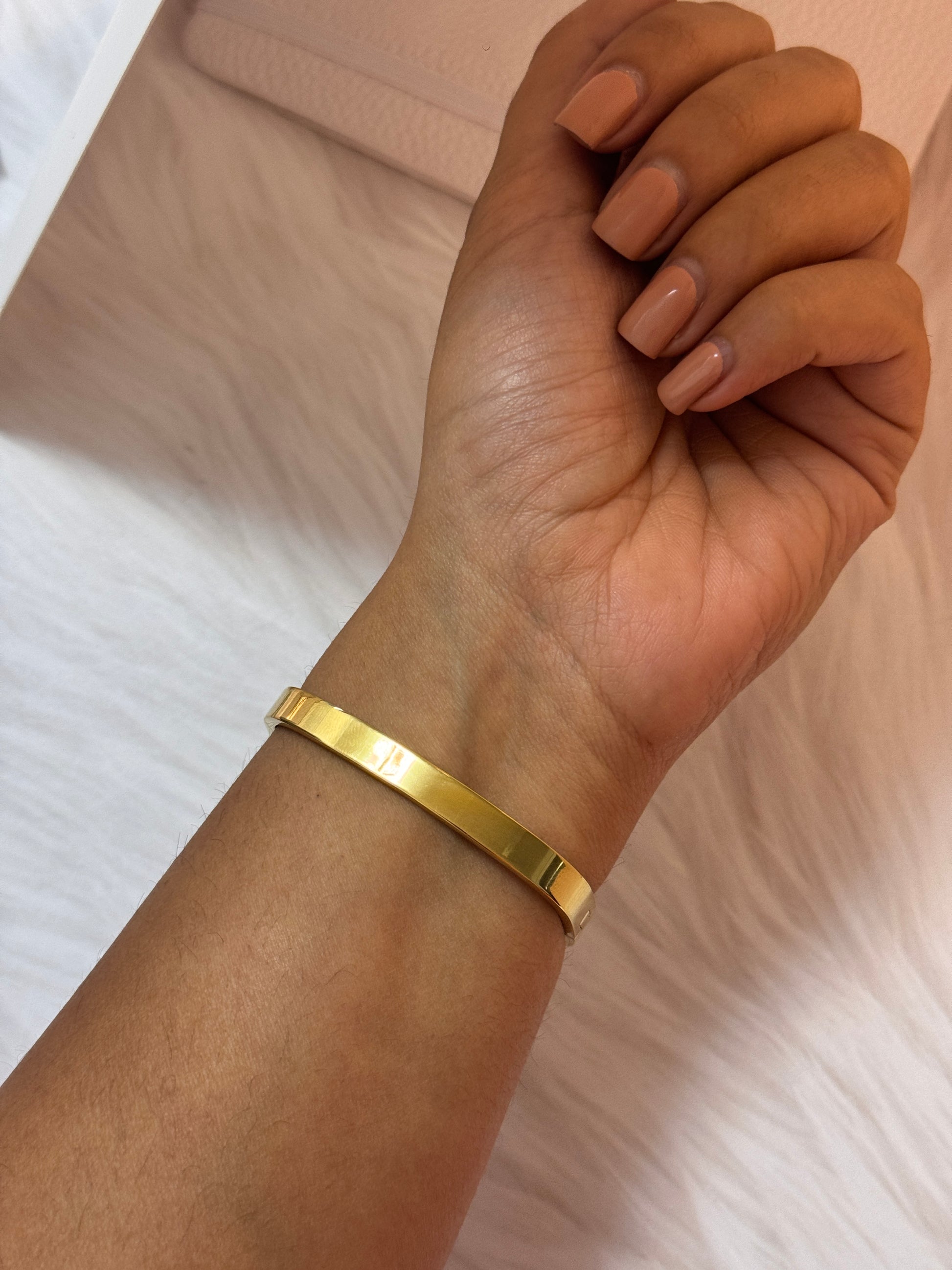 Gold bracelet on a wrist with a neutral background